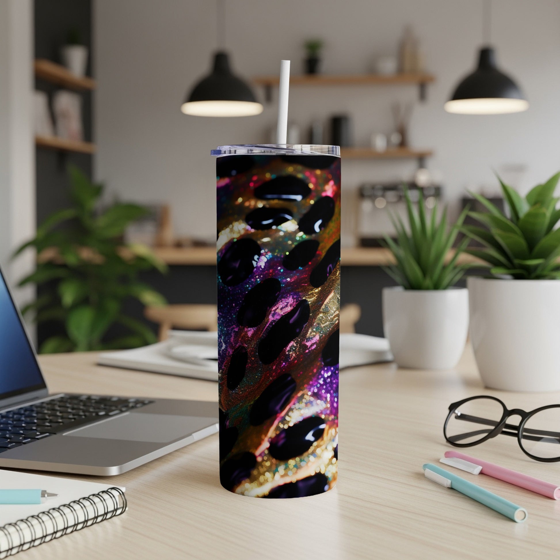 Colorful speckled tumbler with straw on a desk next to a laptop and pens.