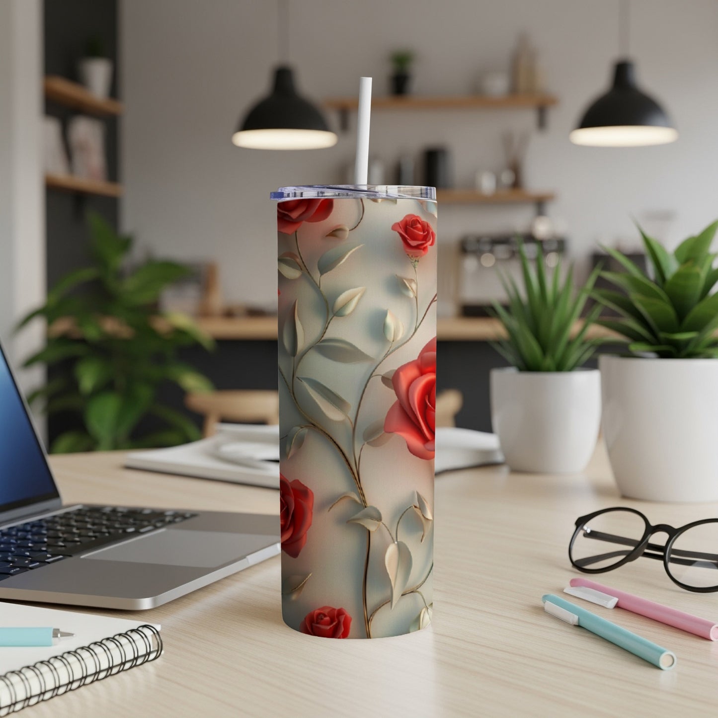 Tall tumbler with red roses and green vine pattern, on a desk.