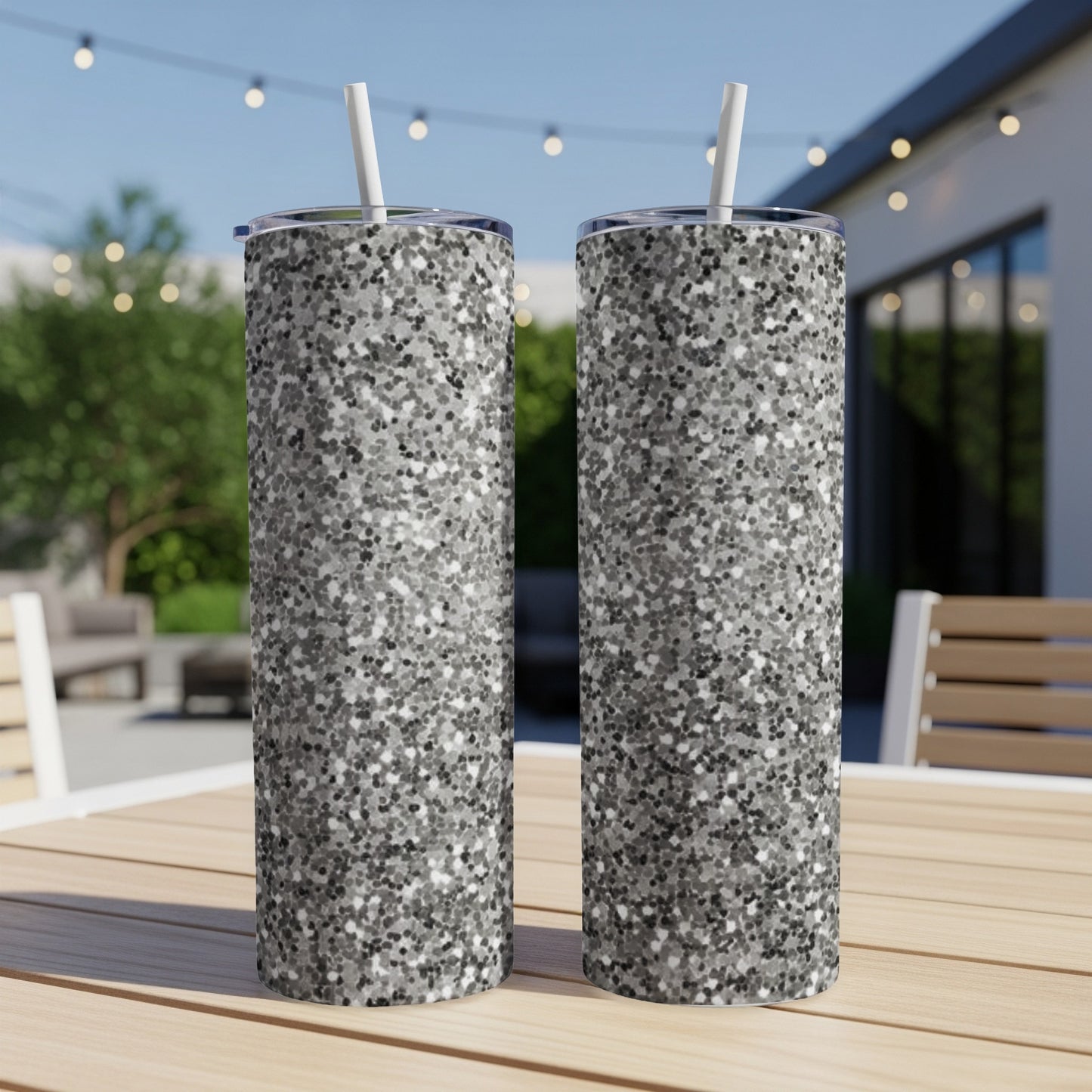 Two silver glitter tumblers with straws on a wooden table.