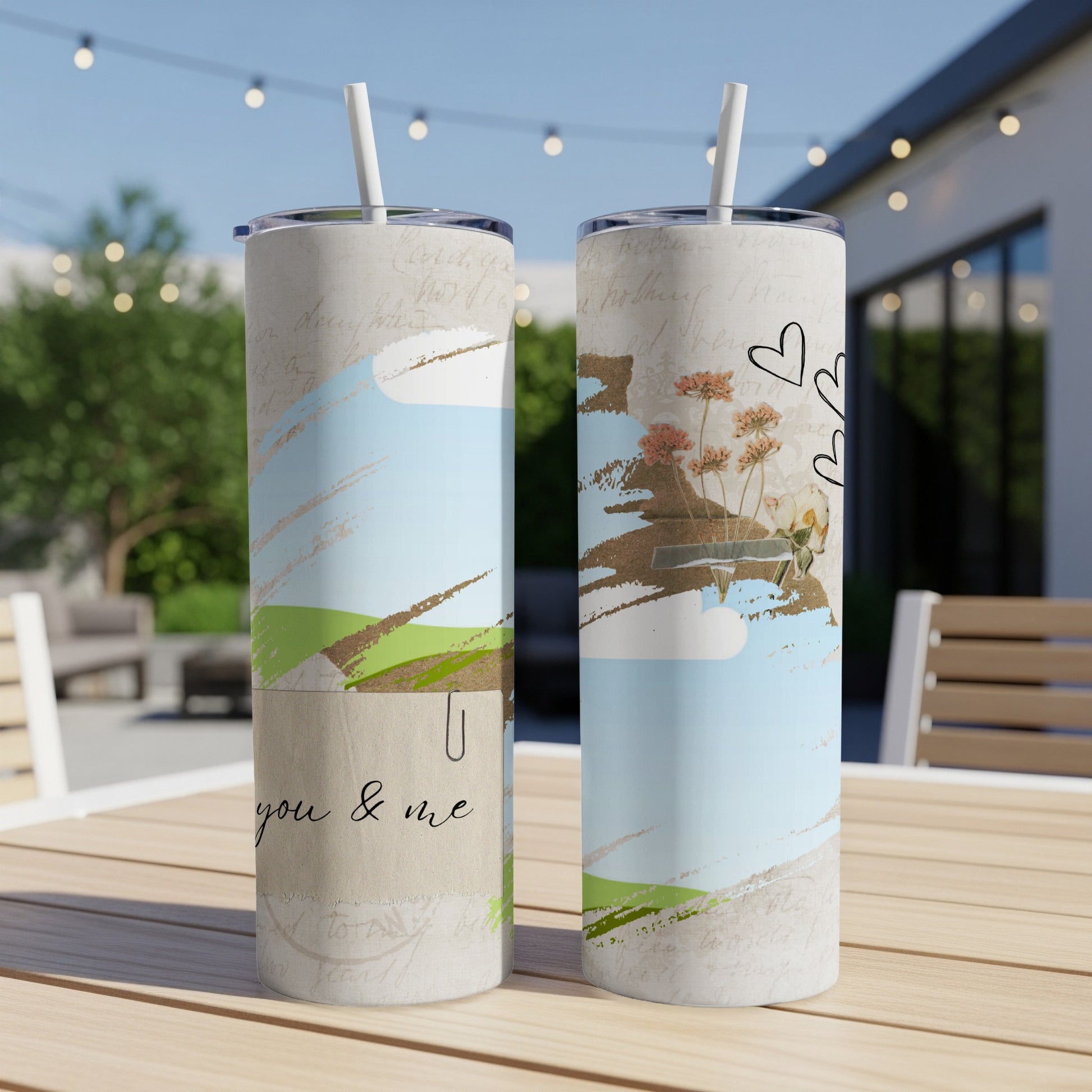 Two tumblers with floral and heart designs on a wooden table outdoors.