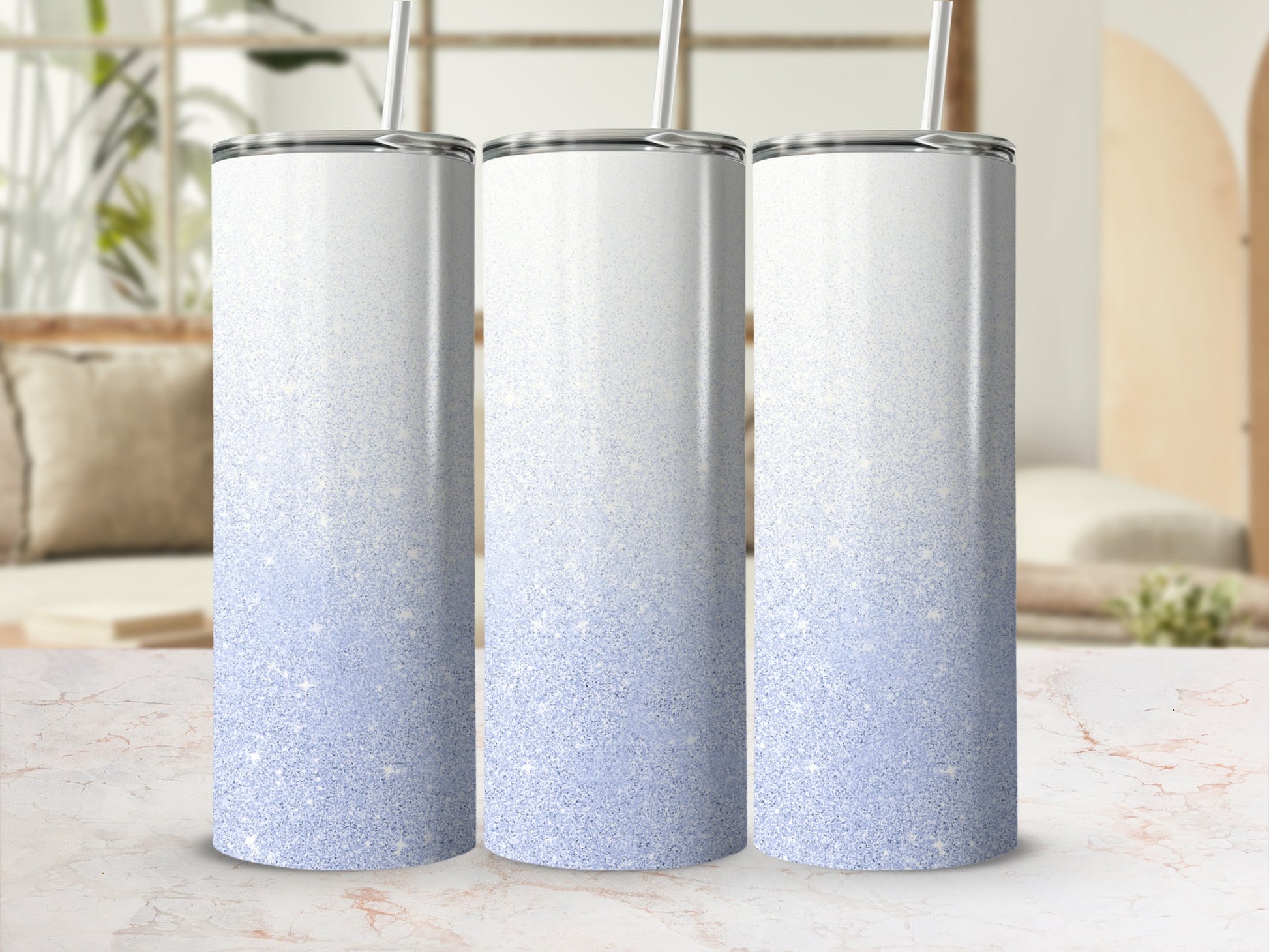 Three white and pale blue glitter tumblers with straws on a marble surface.