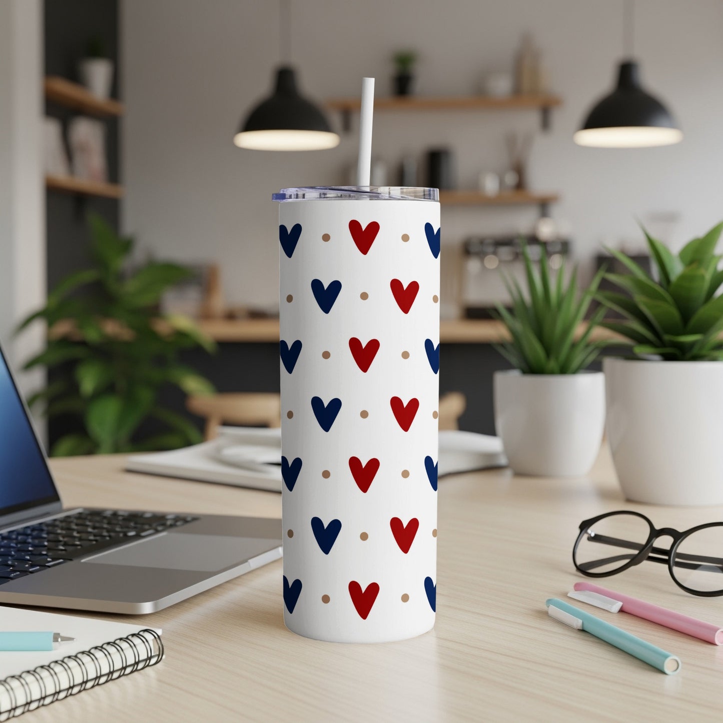 White tumbler with red and blue heart pattern, on a desk.