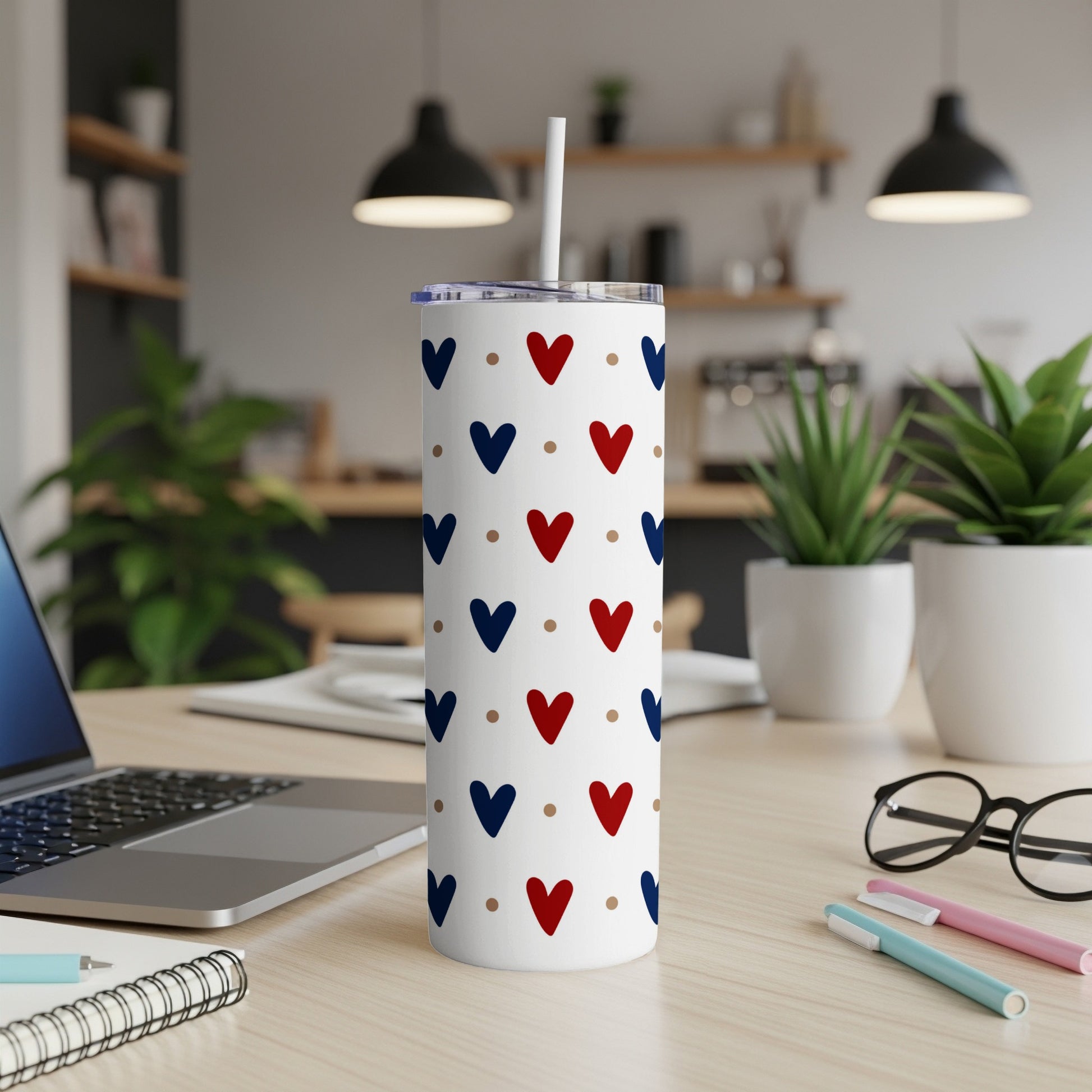 White tumbler with red and blue heart pattern, on a desk.
