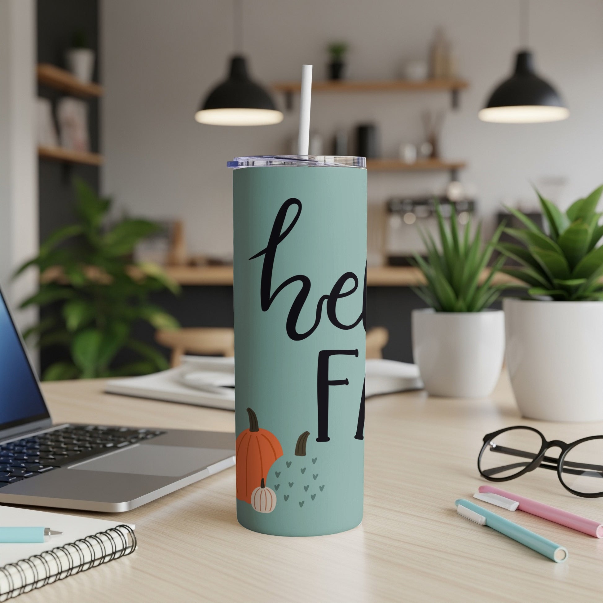 Mint green tumbler with "hello fall" text and pumpkins, on a desk.