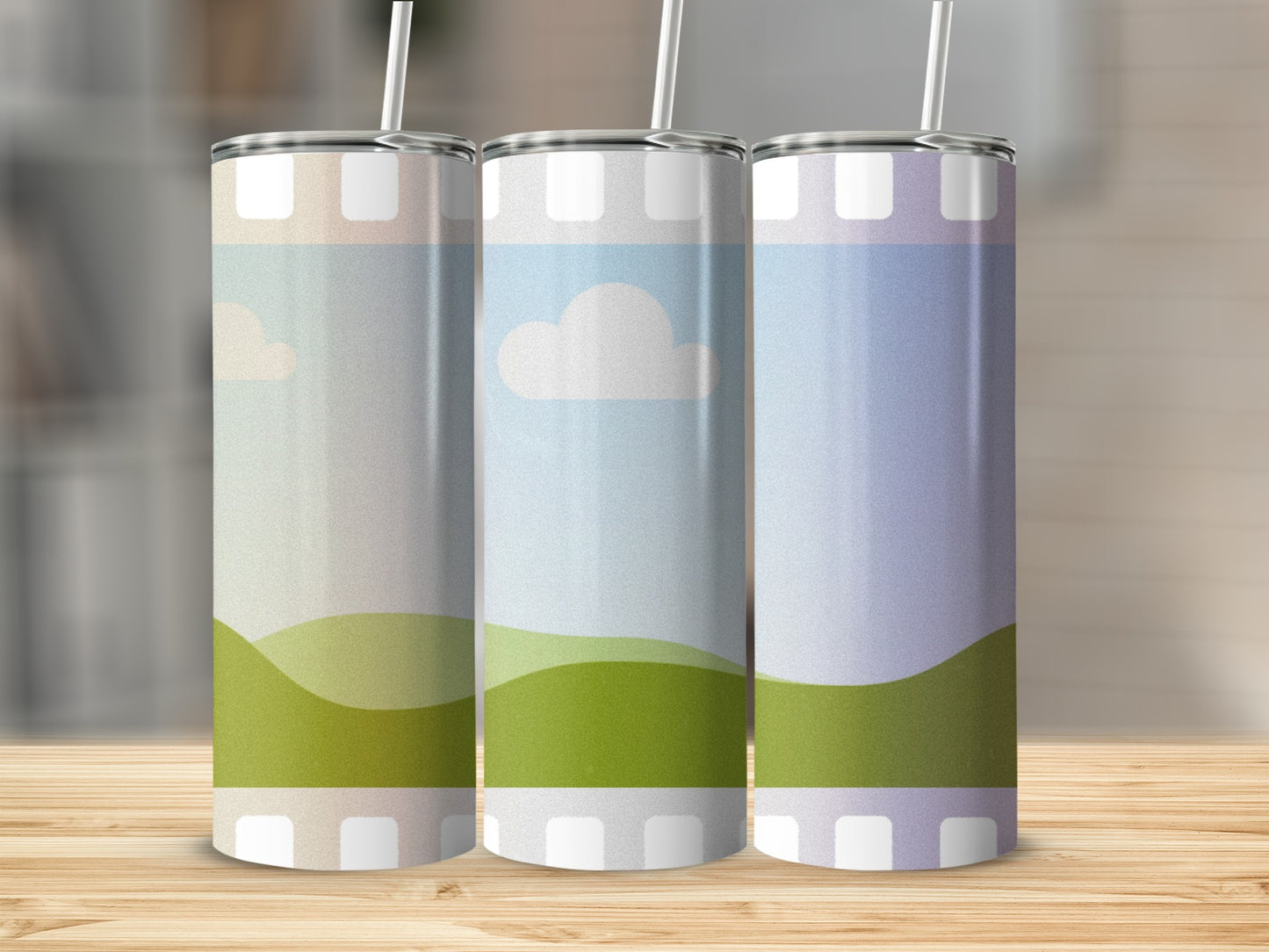 Three tumblers with abstract landscape designs and straws stand on a wooden surface.