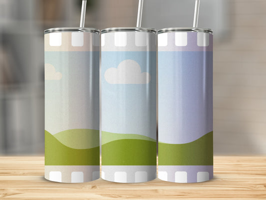 Three tumblers with abstract landscape designs and straws stand on a wooden surface.