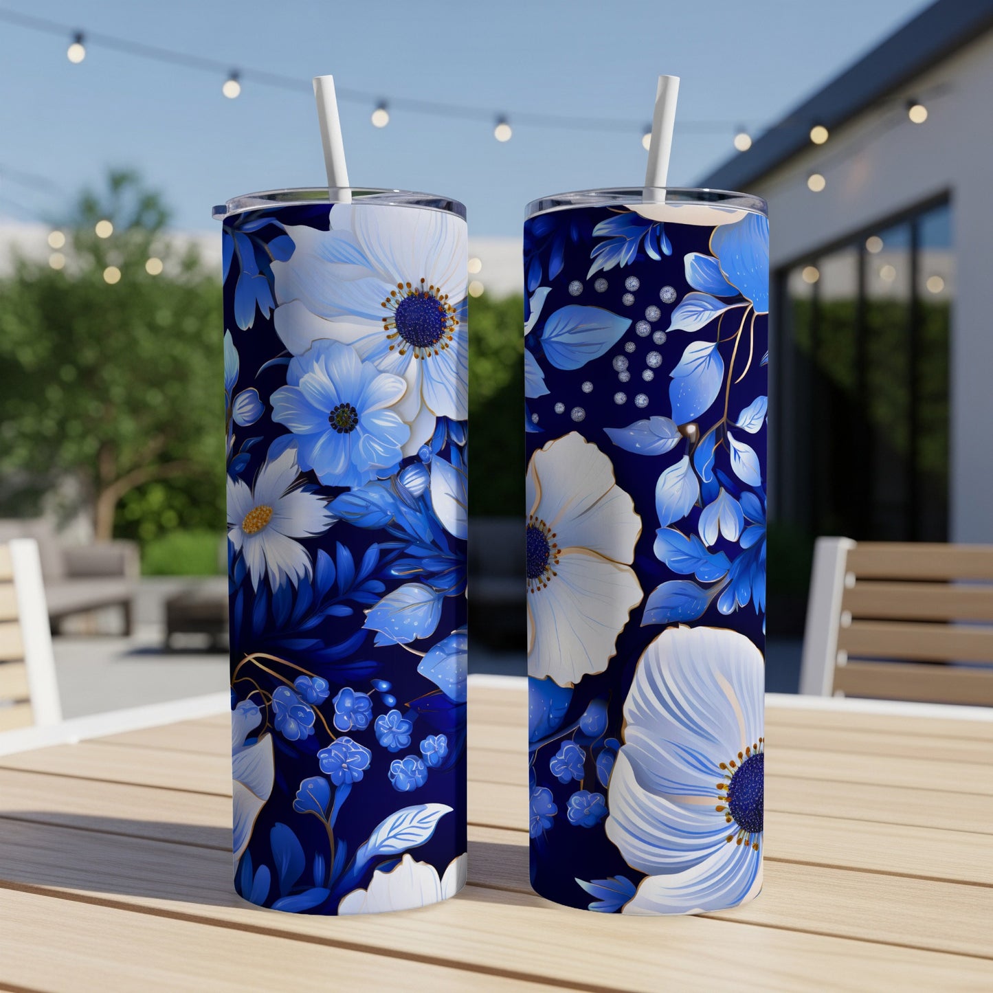 Two blue floral tumblers with straws on a wooden table outdoors.