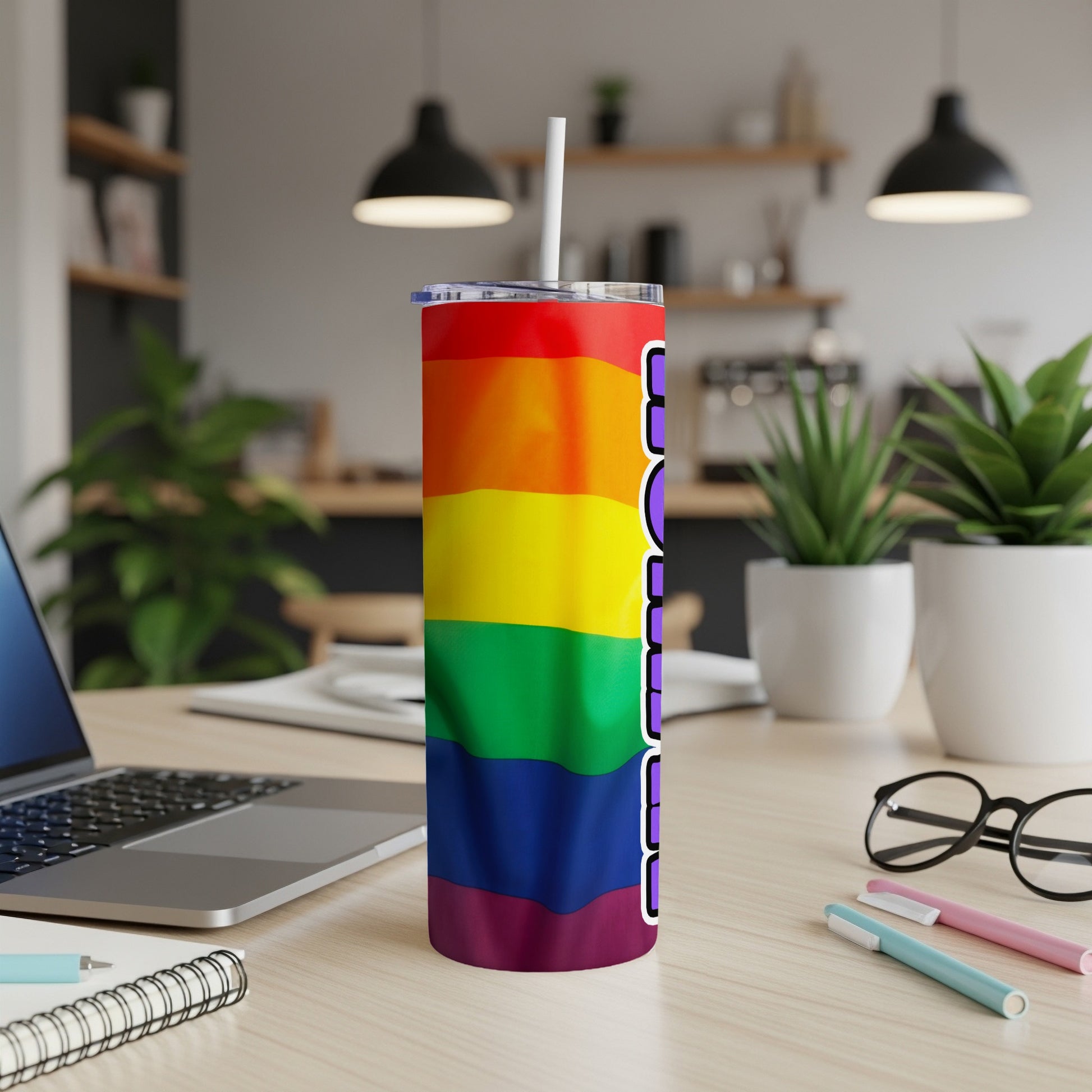 Rainbow pride tumbler with straw on a desk next to a laptop.