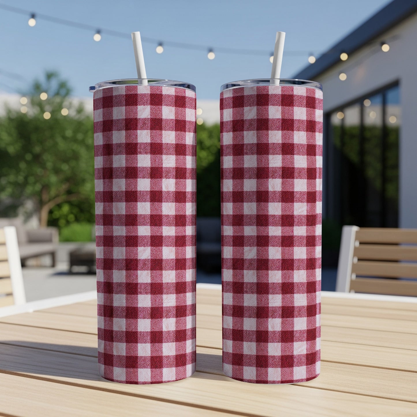 Two red and white checkered tumblers with straws sit on a wooden table outdoors.