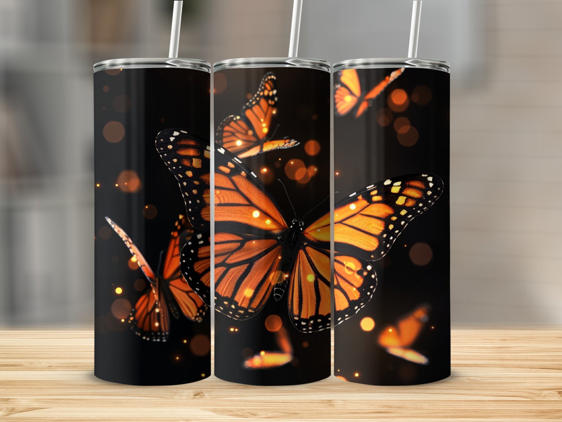 Three tumblers with monarch butterflies and bokeh lights on a wooden surface.