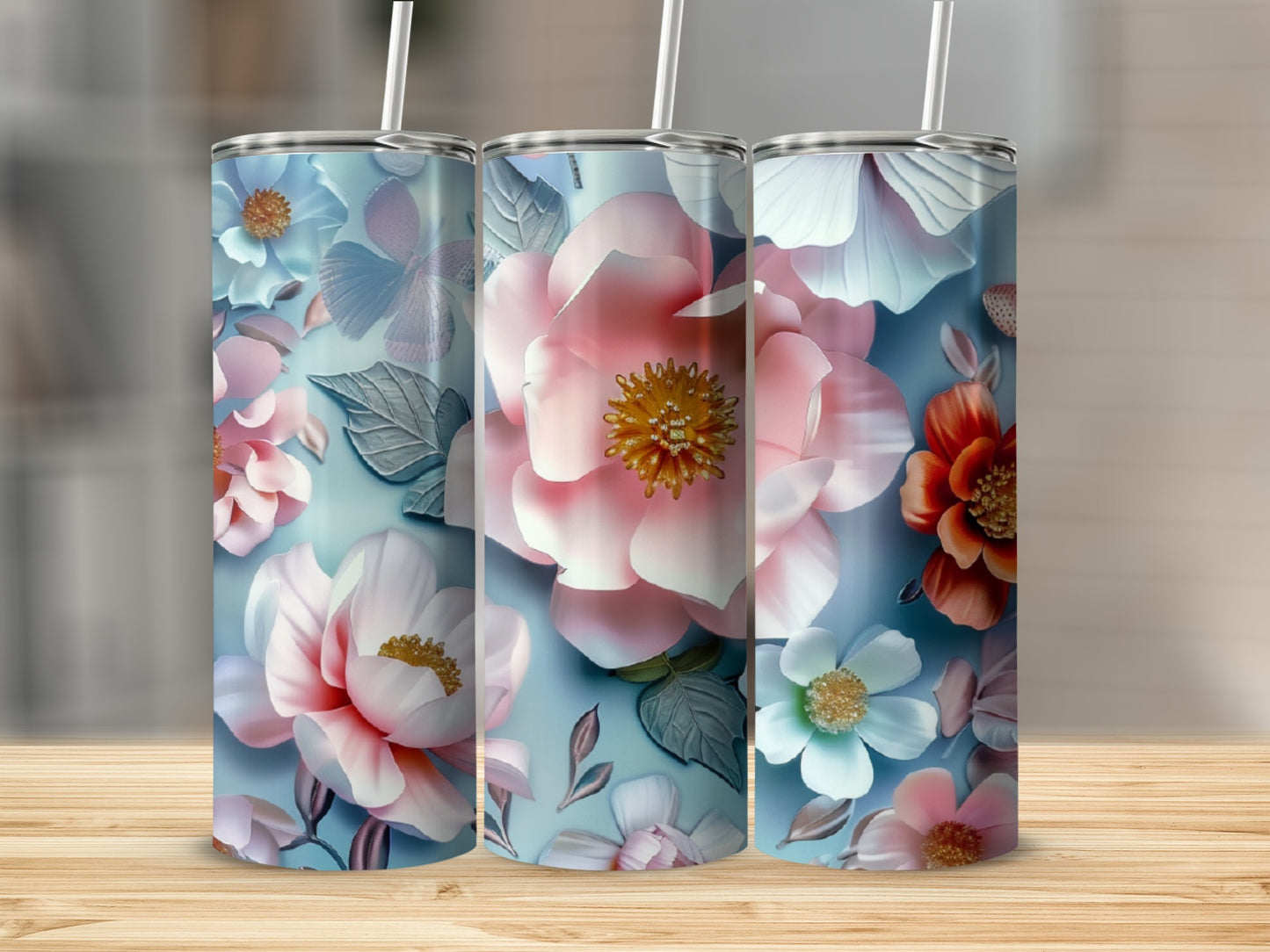 Three tumblers with a light blue background and various pink, white, and orange floral designs.
