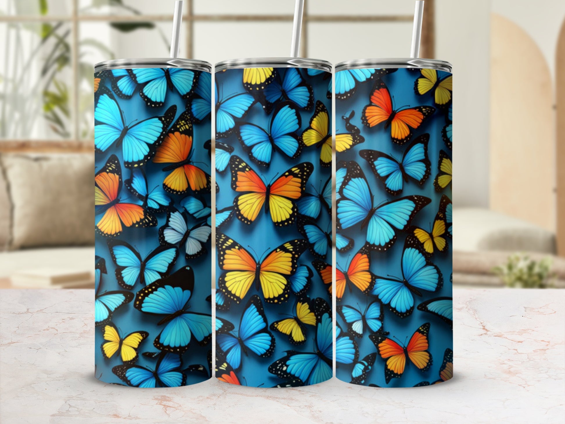 Three blue tumblers with colorful butterfly designs against a blurred indoor background.