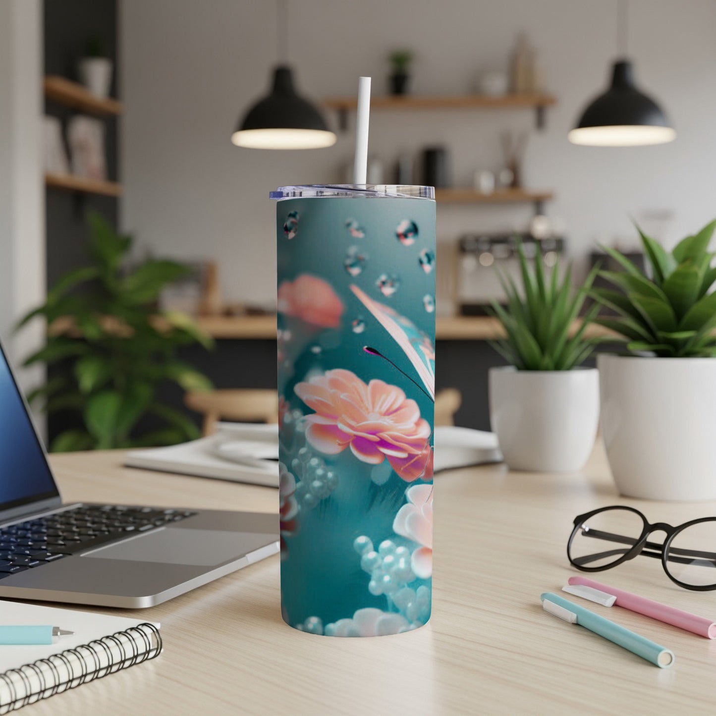 Teal tumbler with floral and bubble design, on a desk.