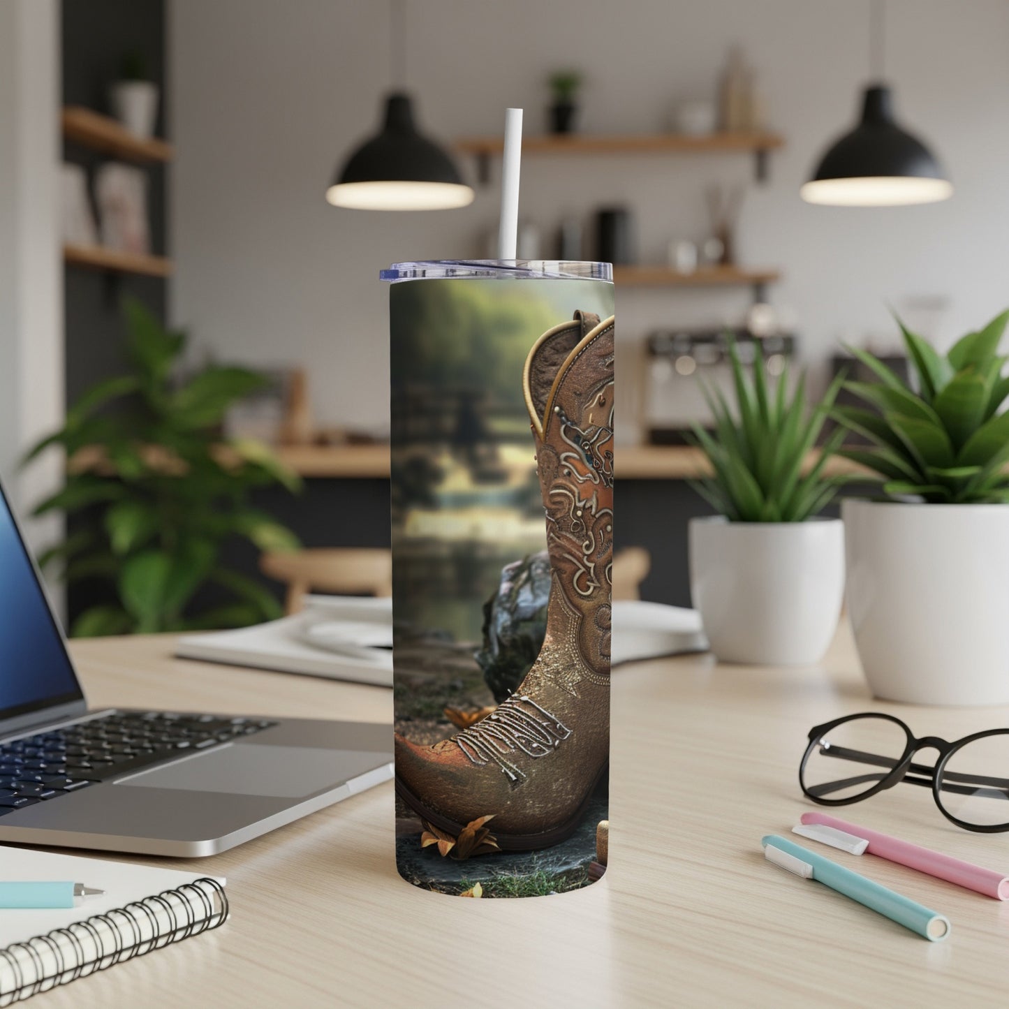 Cowboy boot on a wooden table with a laptop and office supplies.