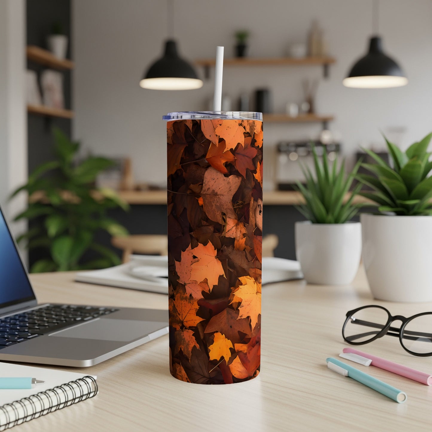 Tumbler with autumn leaf pattern on a desk with a laptop.