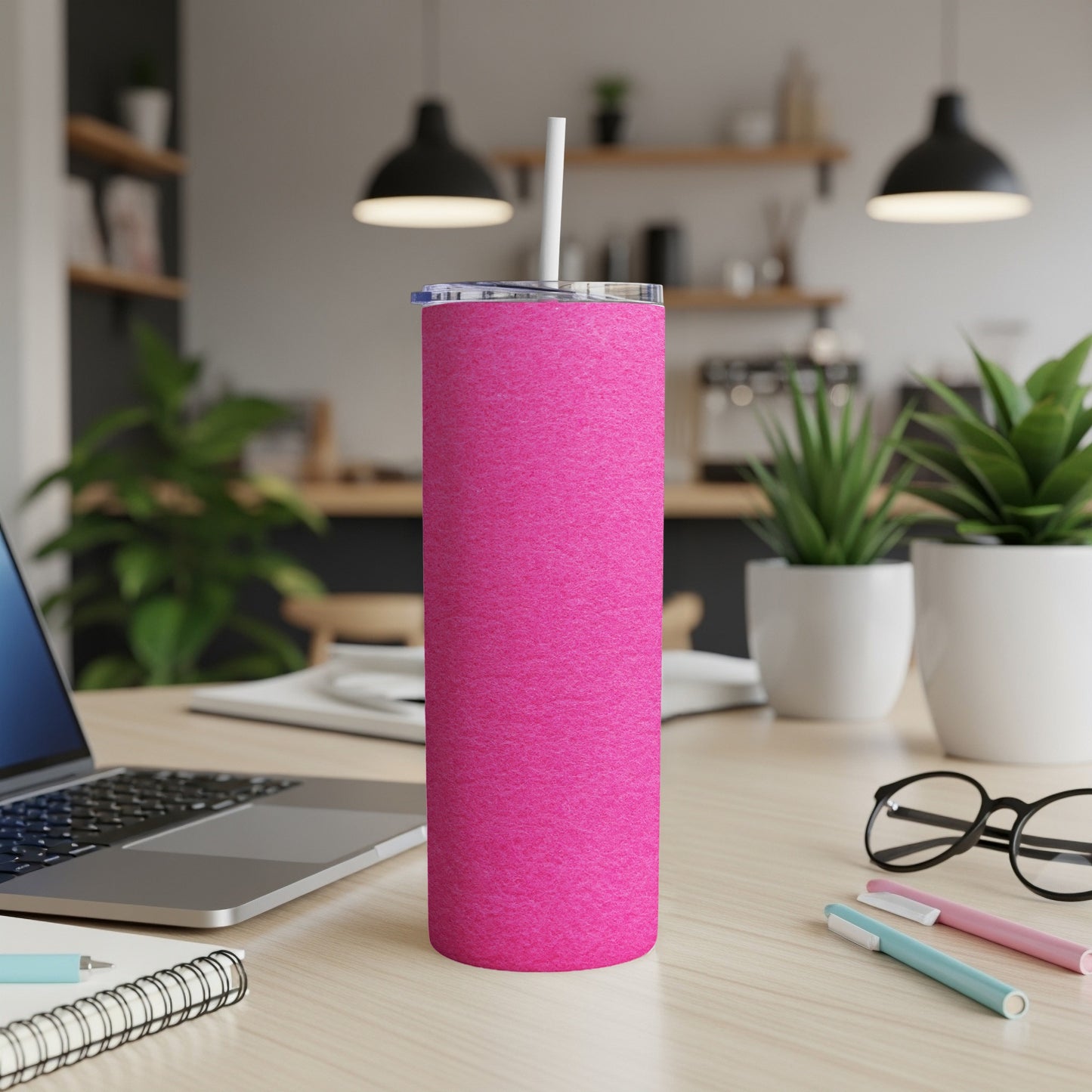 Pink textured tumbler with white straw on a desk with laptop and pens.