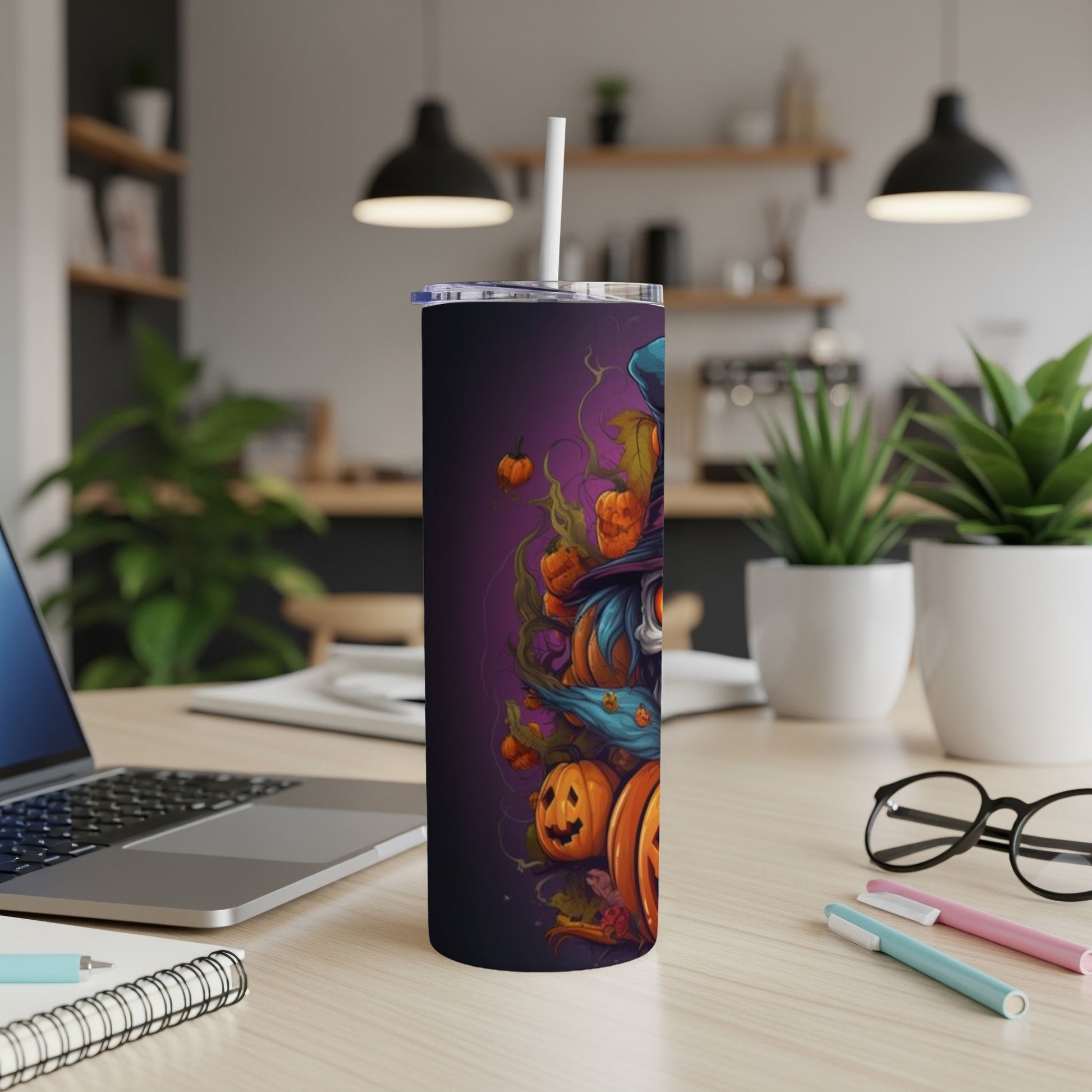 Tumbler with Halloween witch and pumpkins design, on a desk with laptop and plants.