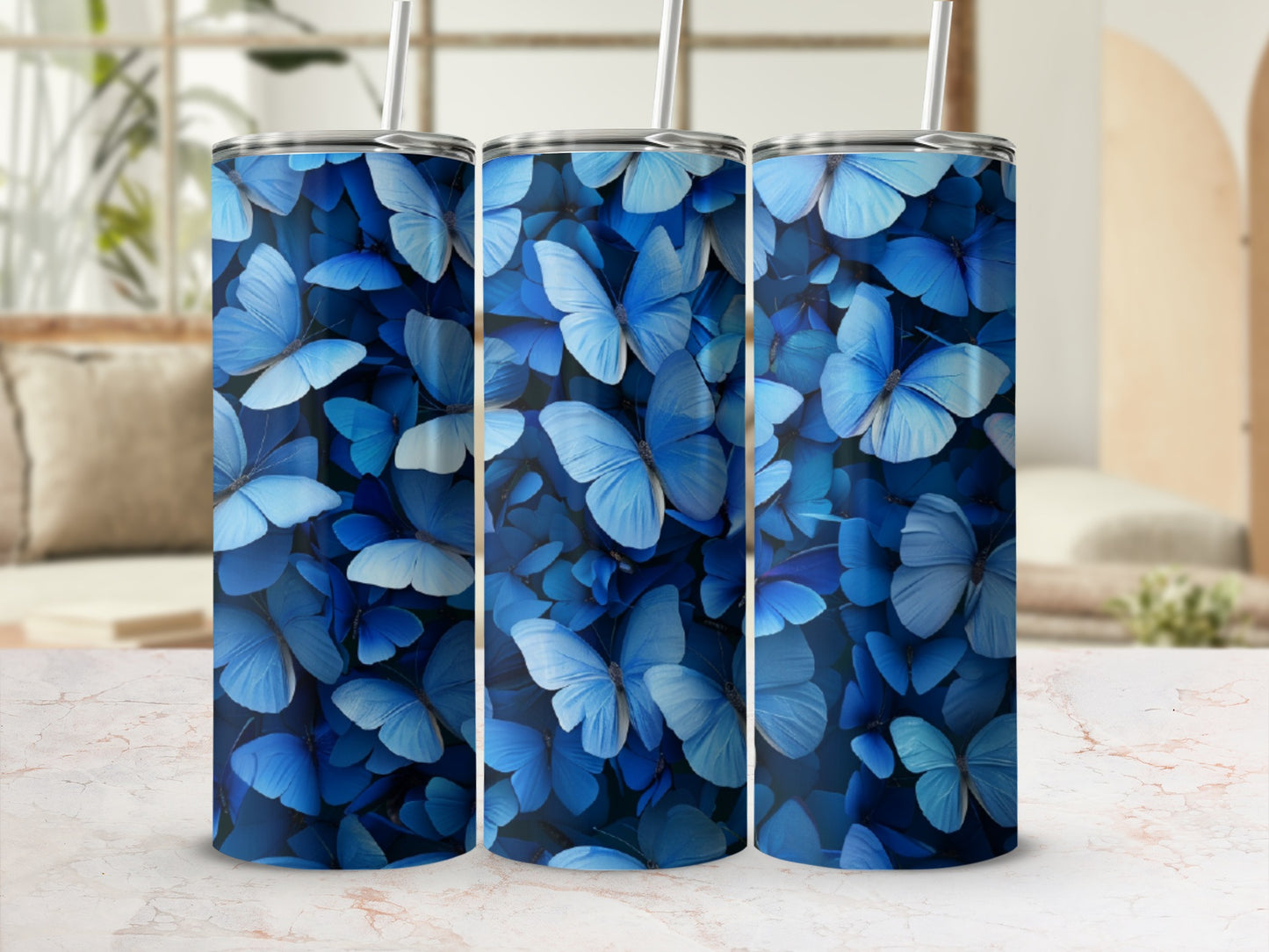 Three blue butterfly patterned tumblers with straws on a marble surface.