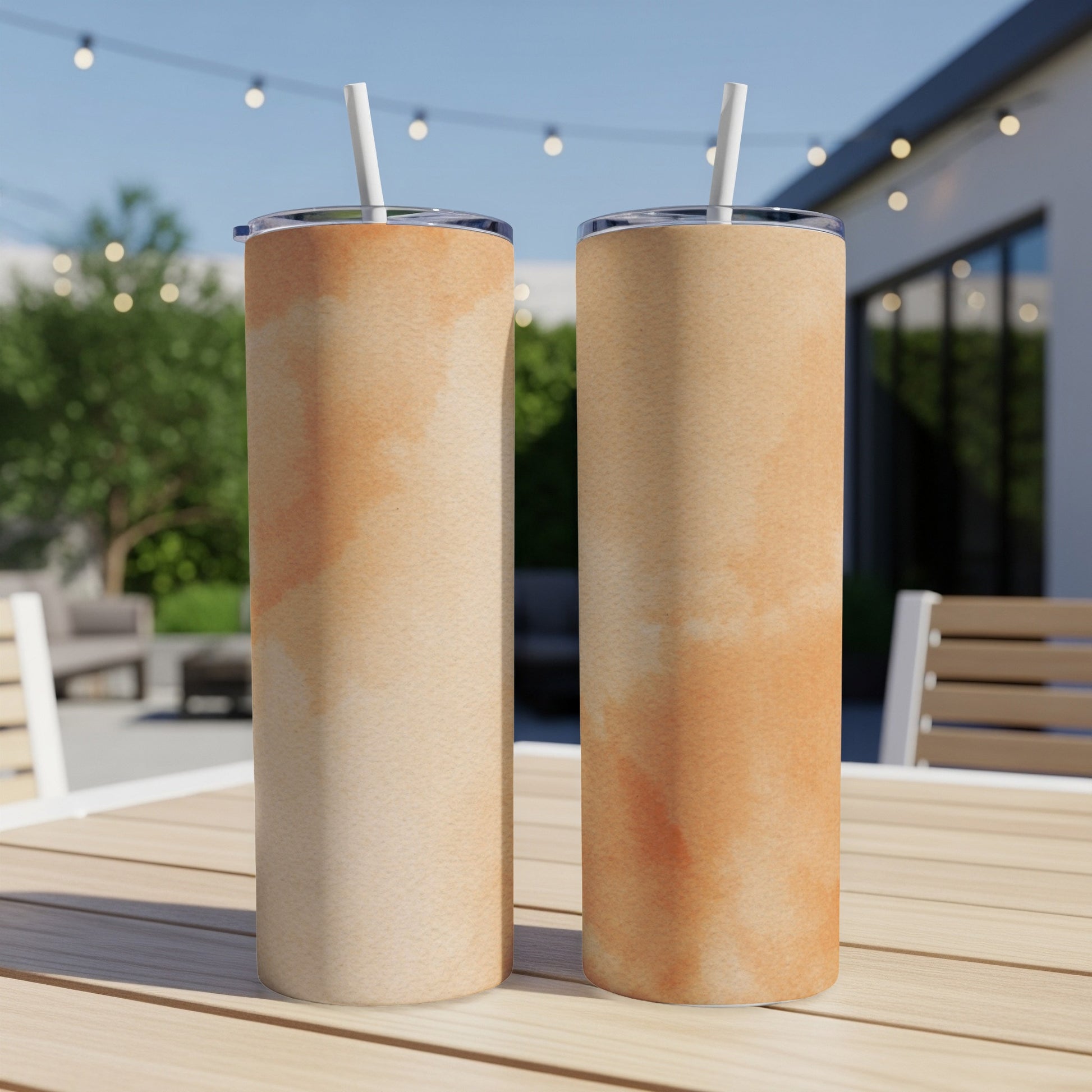 Two tan tumblers with subtle orange watercolor designs on a wooden table.