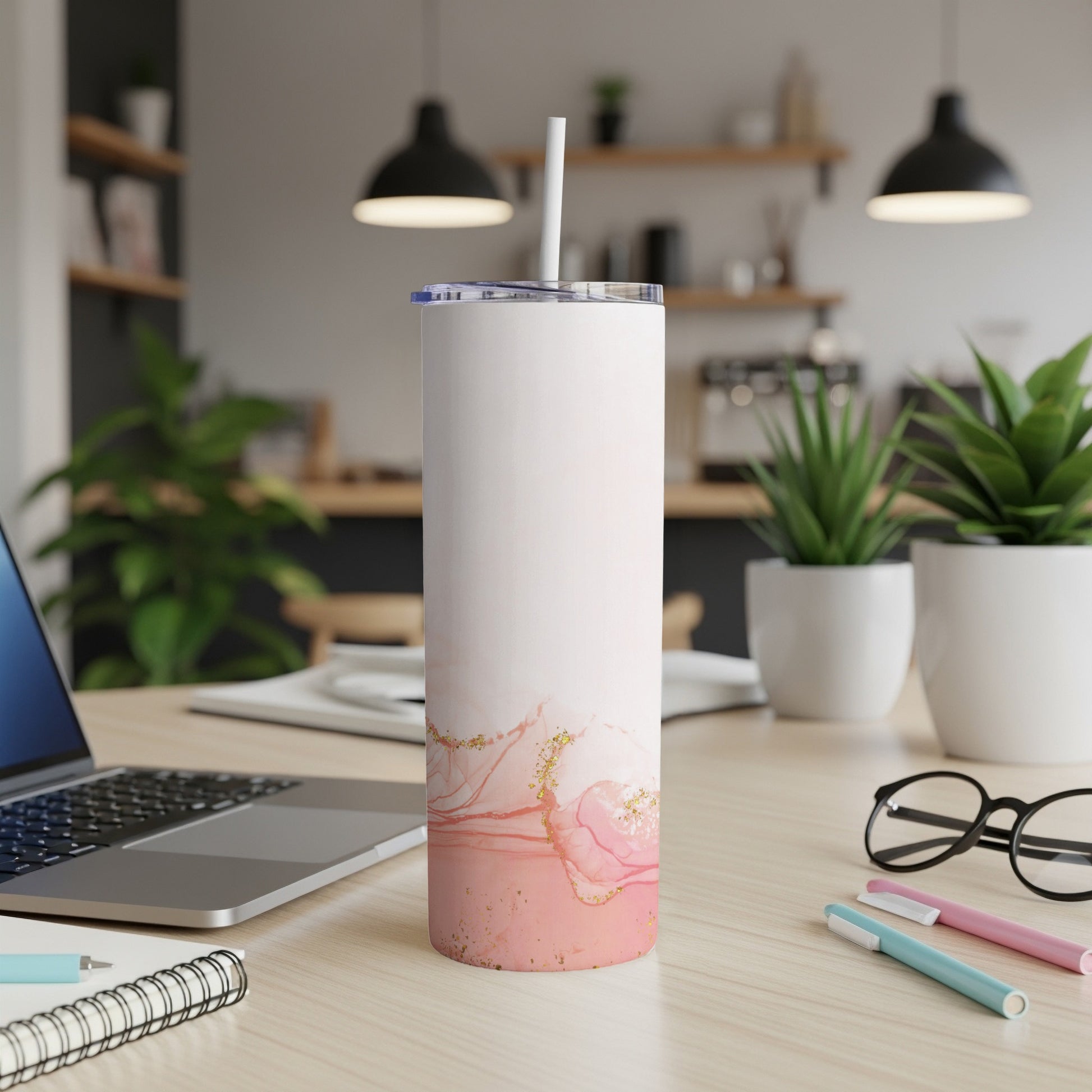Pink marble tumbler with gold accents on a desk with a laptop.