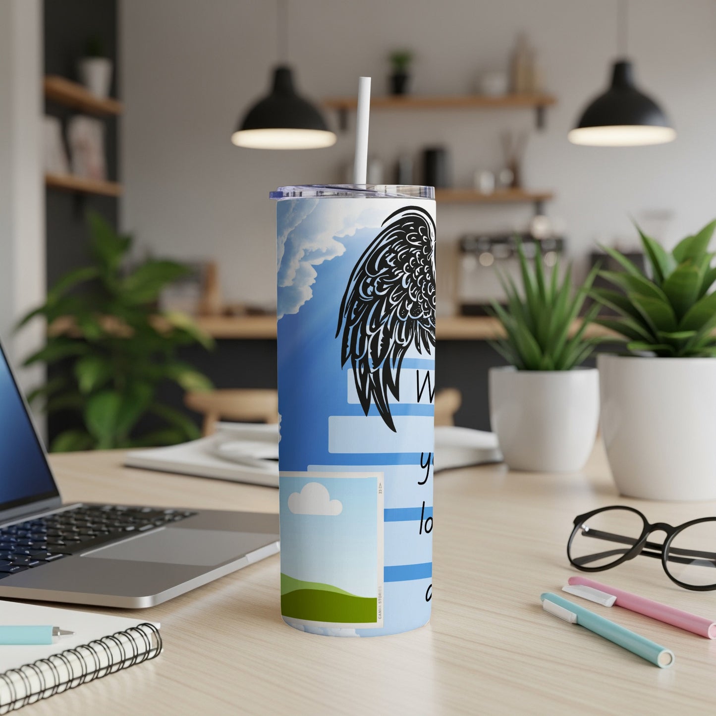 Tumbler with black wings, clouds, and text reading "When you're lost" on a desk.