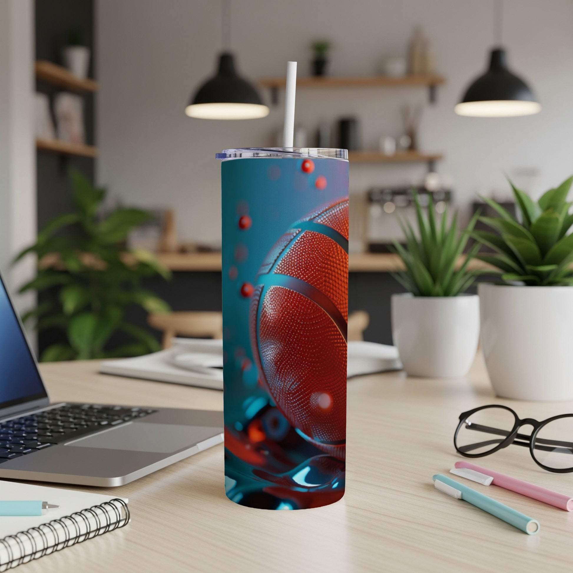 Tumbler with basketball design and straw on a desk with laptop and office supplies.