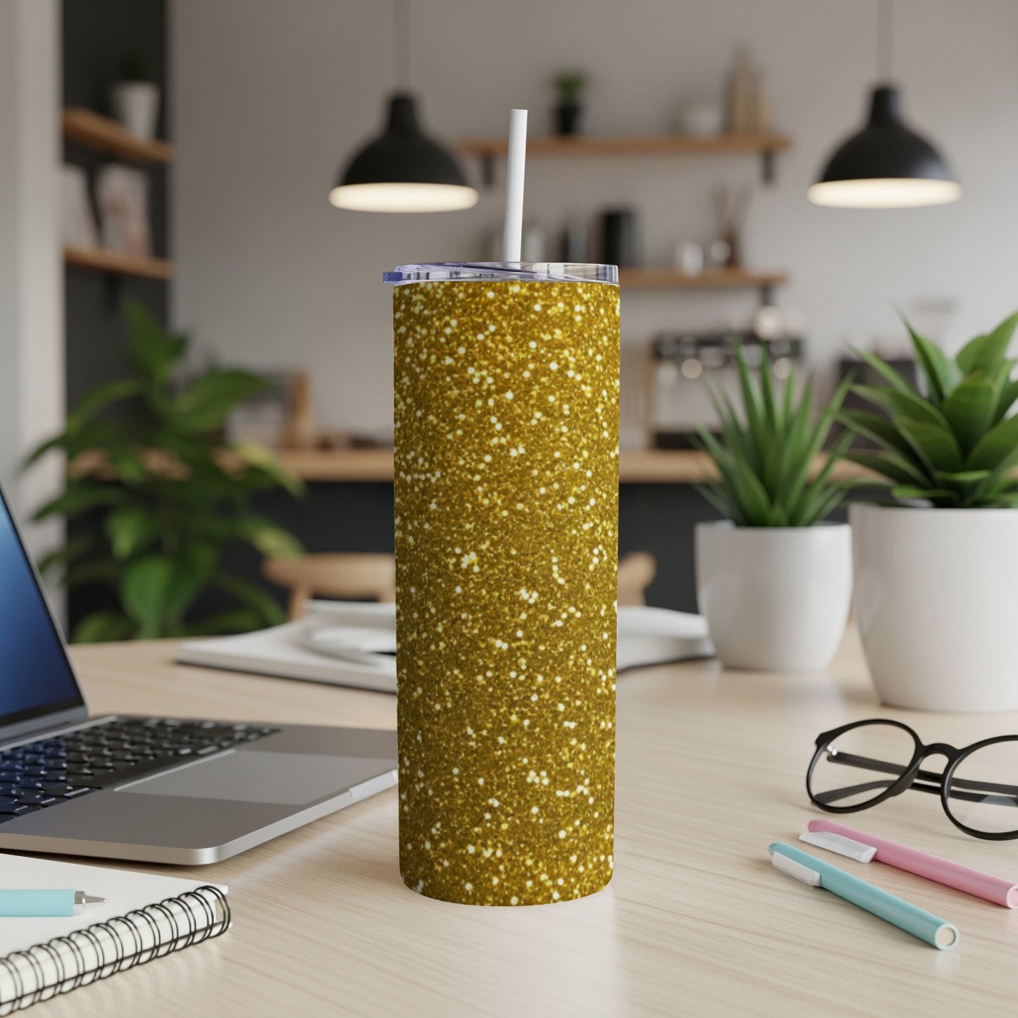 Gold glitter tumbler with straw on a desk with laptop and plants.