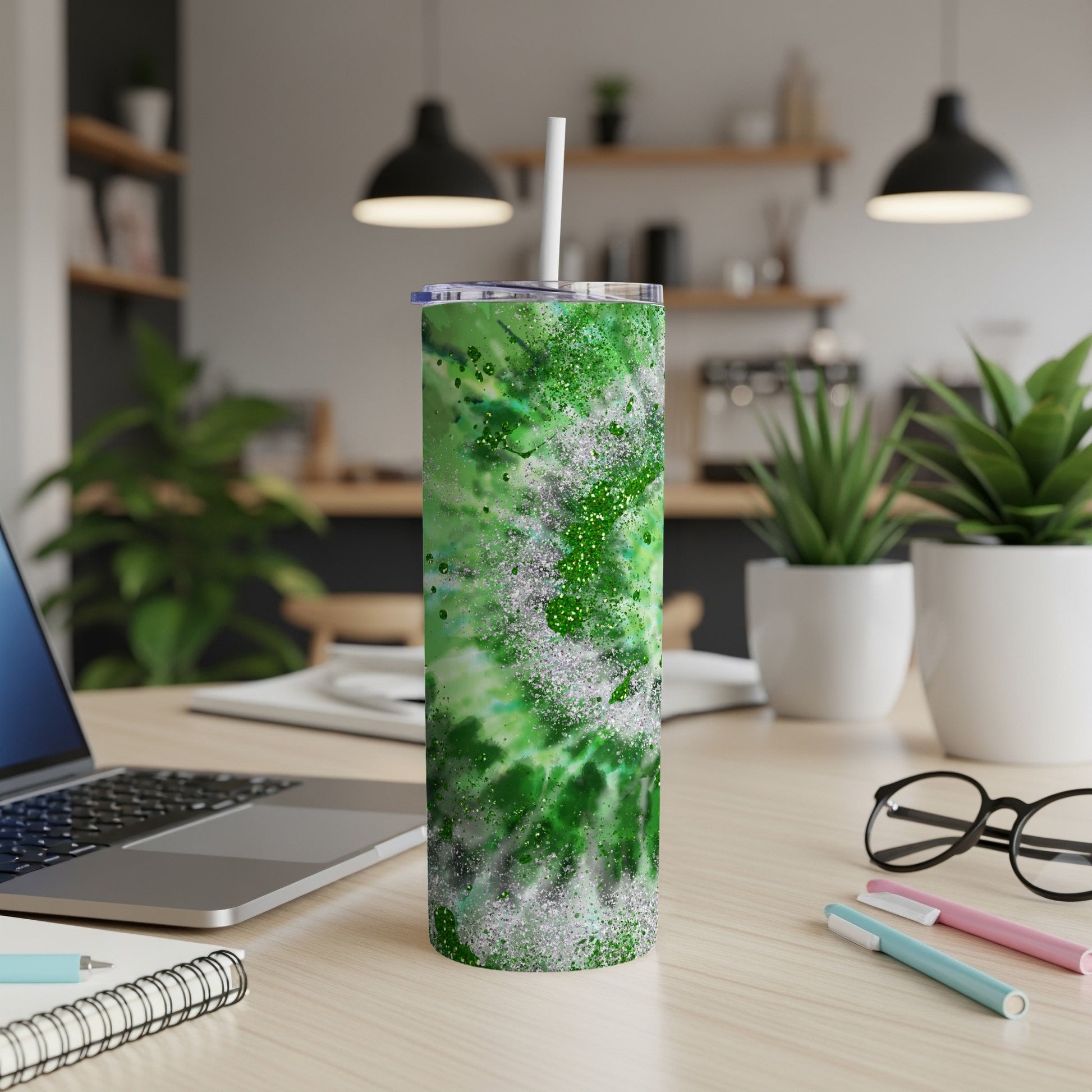 Green tie-dye tumbler with glitter accents, resting on a desk.
