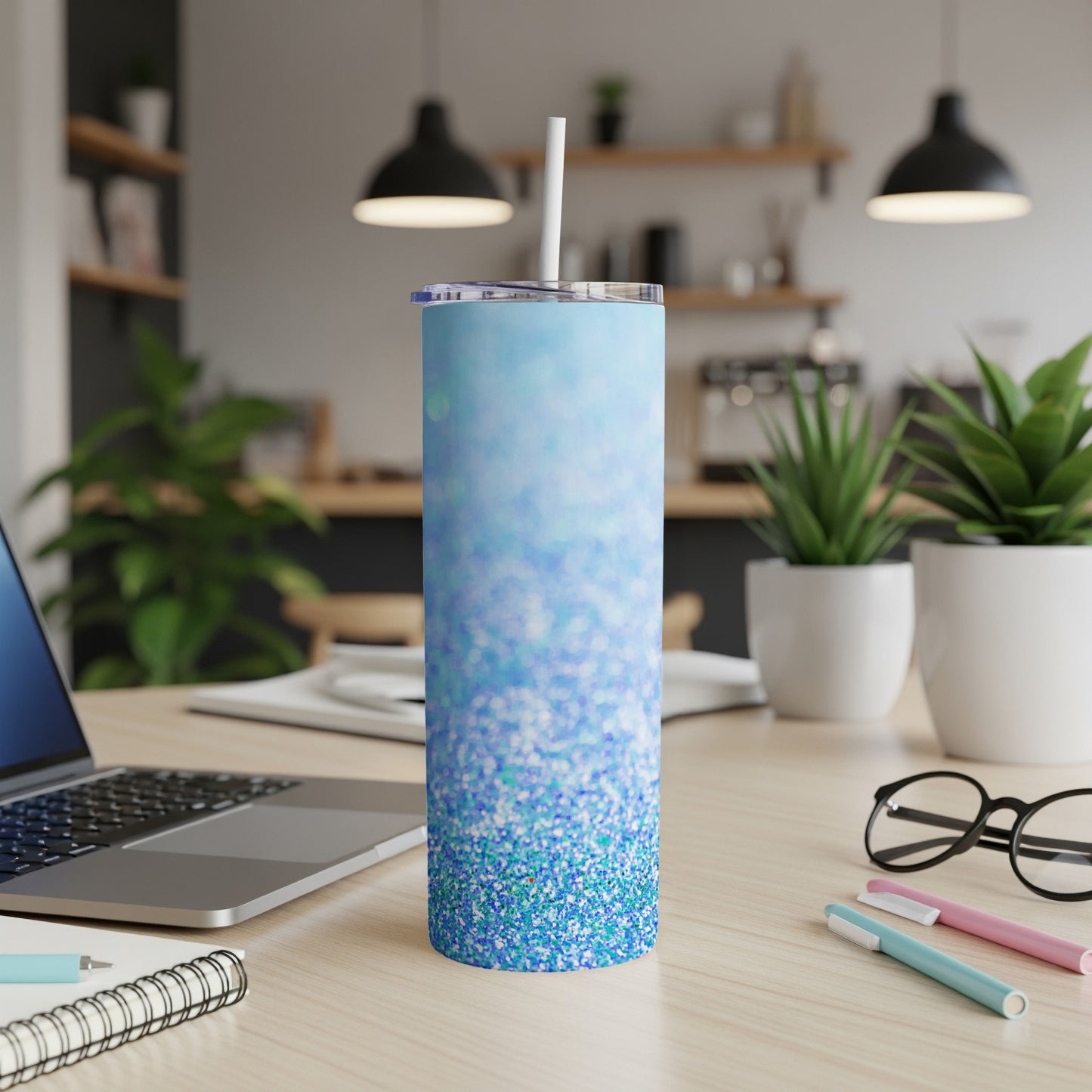 Blue glitter tumbler with white straw on a desk with a laptop and pens.