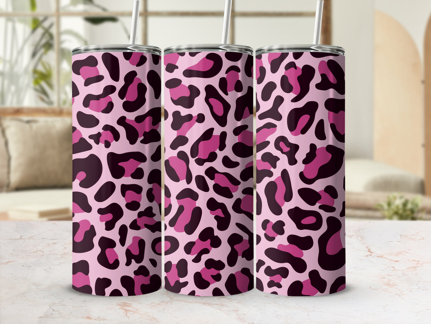 Three tumblers with pink leopard print and straws against a blurred background.