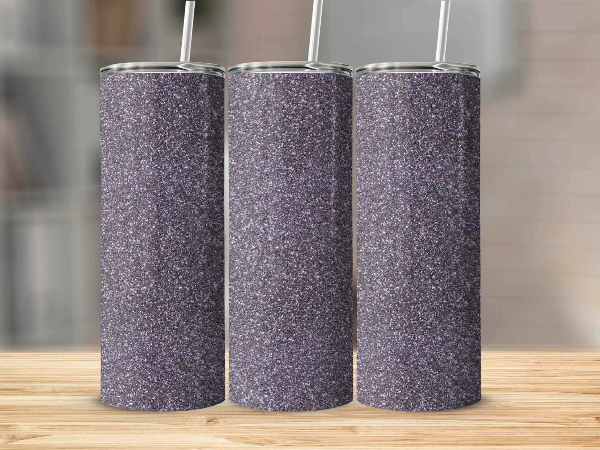 Three glitter tumblers with straws on a wooden surface.