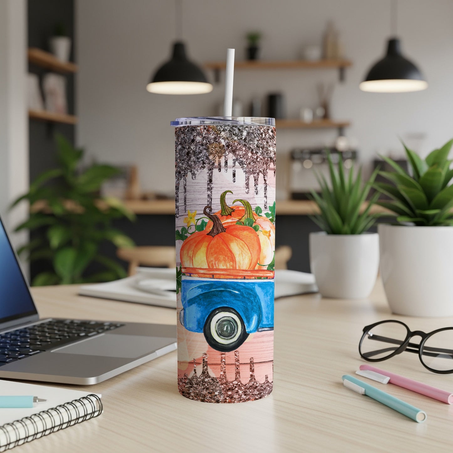 Tumbler with pumpkins on a blue truck, glitter accents, on a wooden desk.