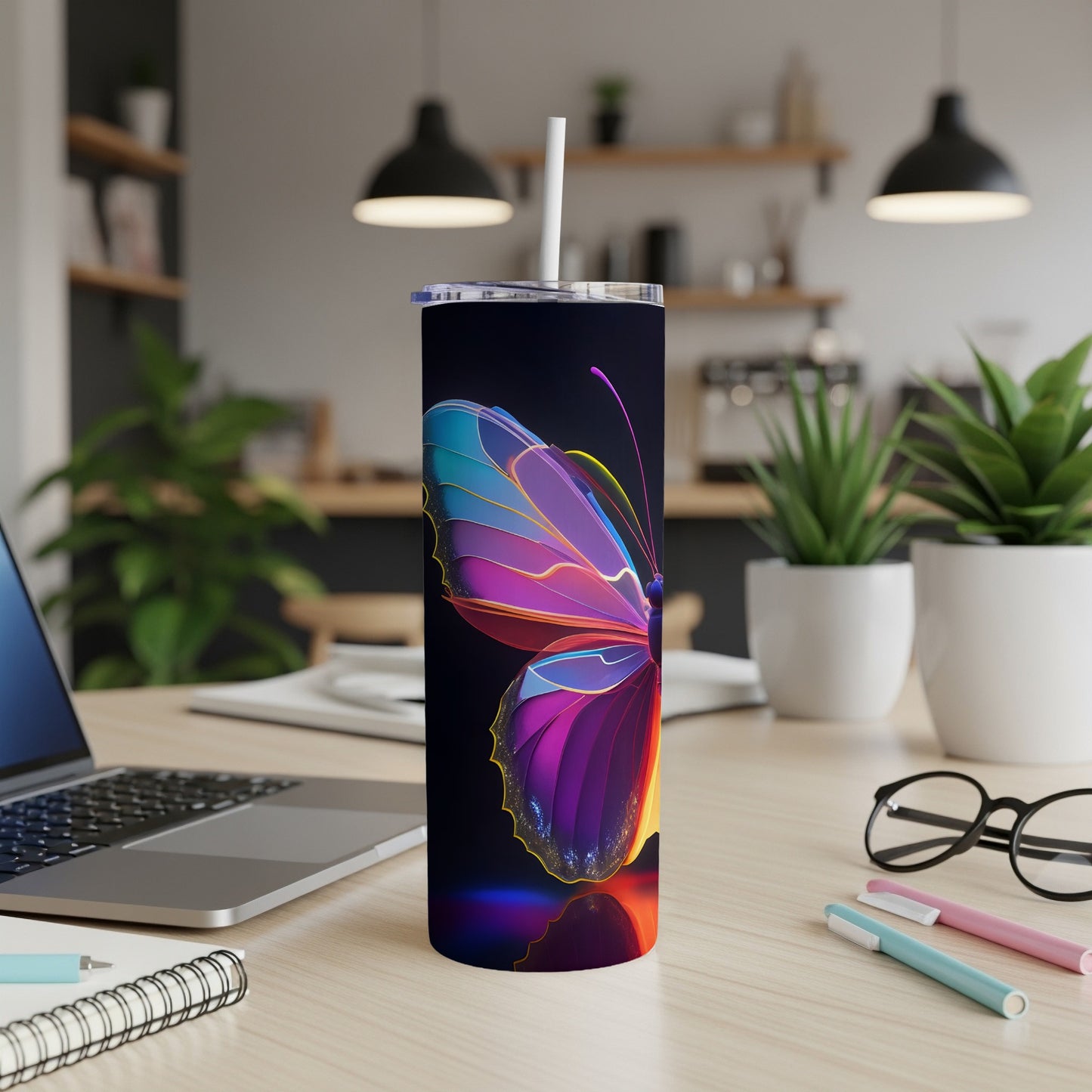 Tumbler with colorful butterfly design, on a desk with laptop and pens.