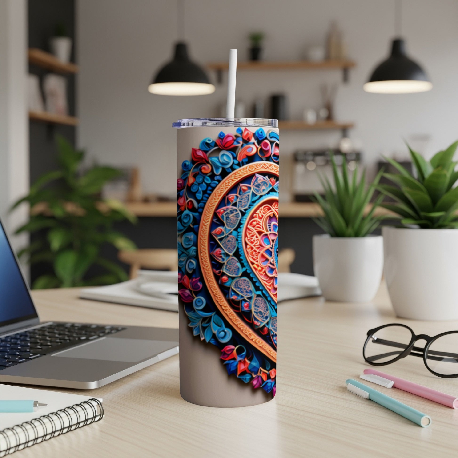 Floral mandala tumbler with straw on desk with laptop and plants.