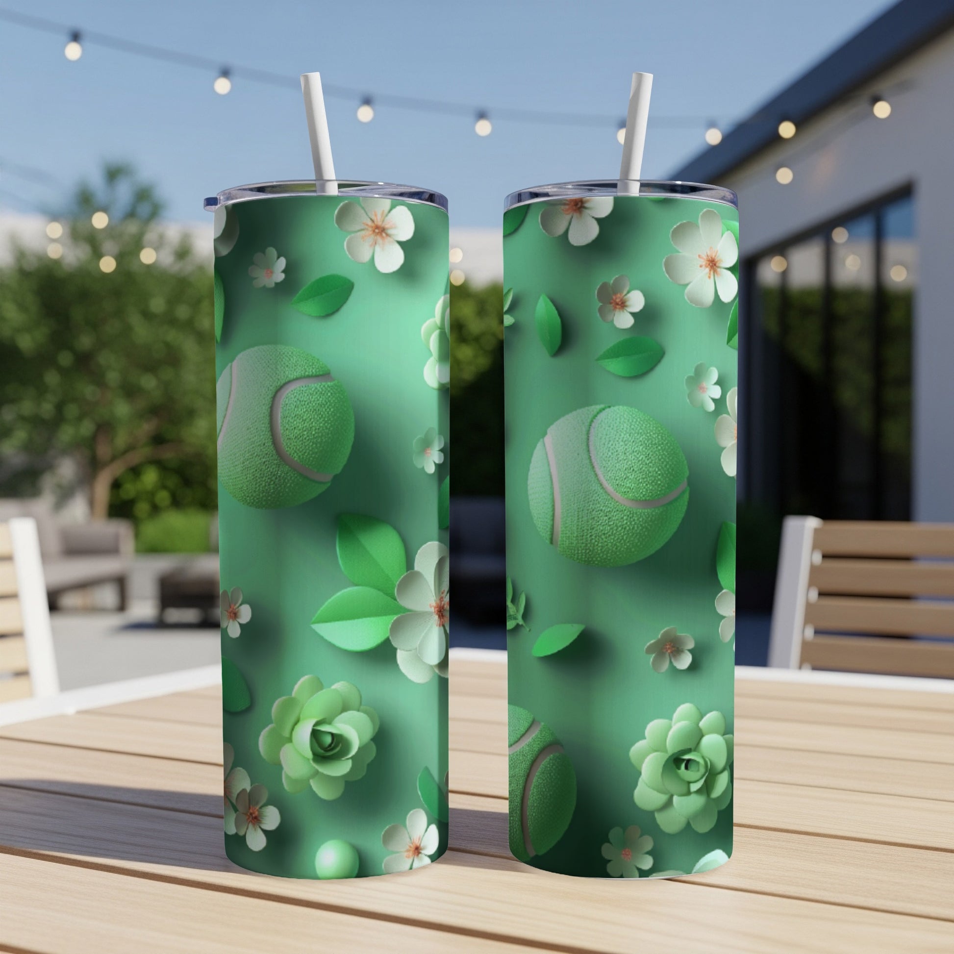 Two green tumblers with tennis balls and floral designs on outdoor table.
