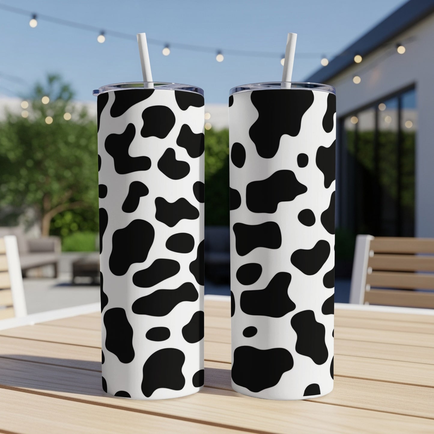 Two tumblers with black and white cow print pattern sit on a wooden table.