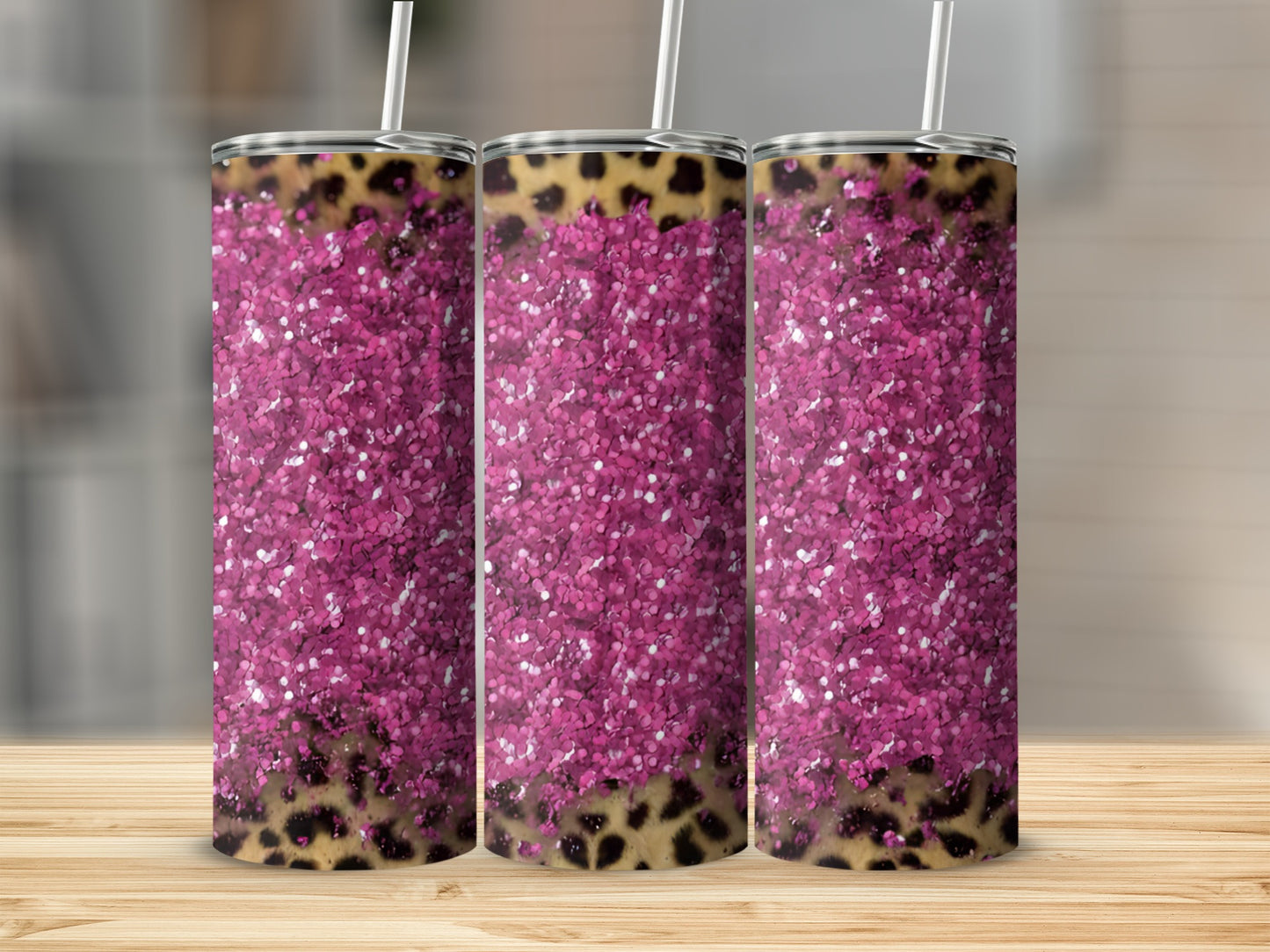Pink glitter and leopard print tumbler with straw on wooden surface.