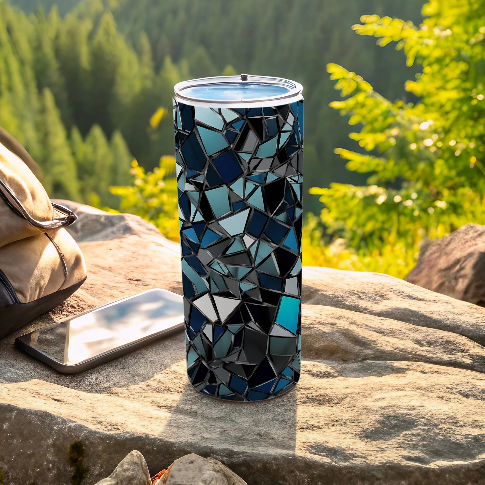 Tall tumbler with geometric blue and black mosaic pattern, outdoors with phone and bag.
