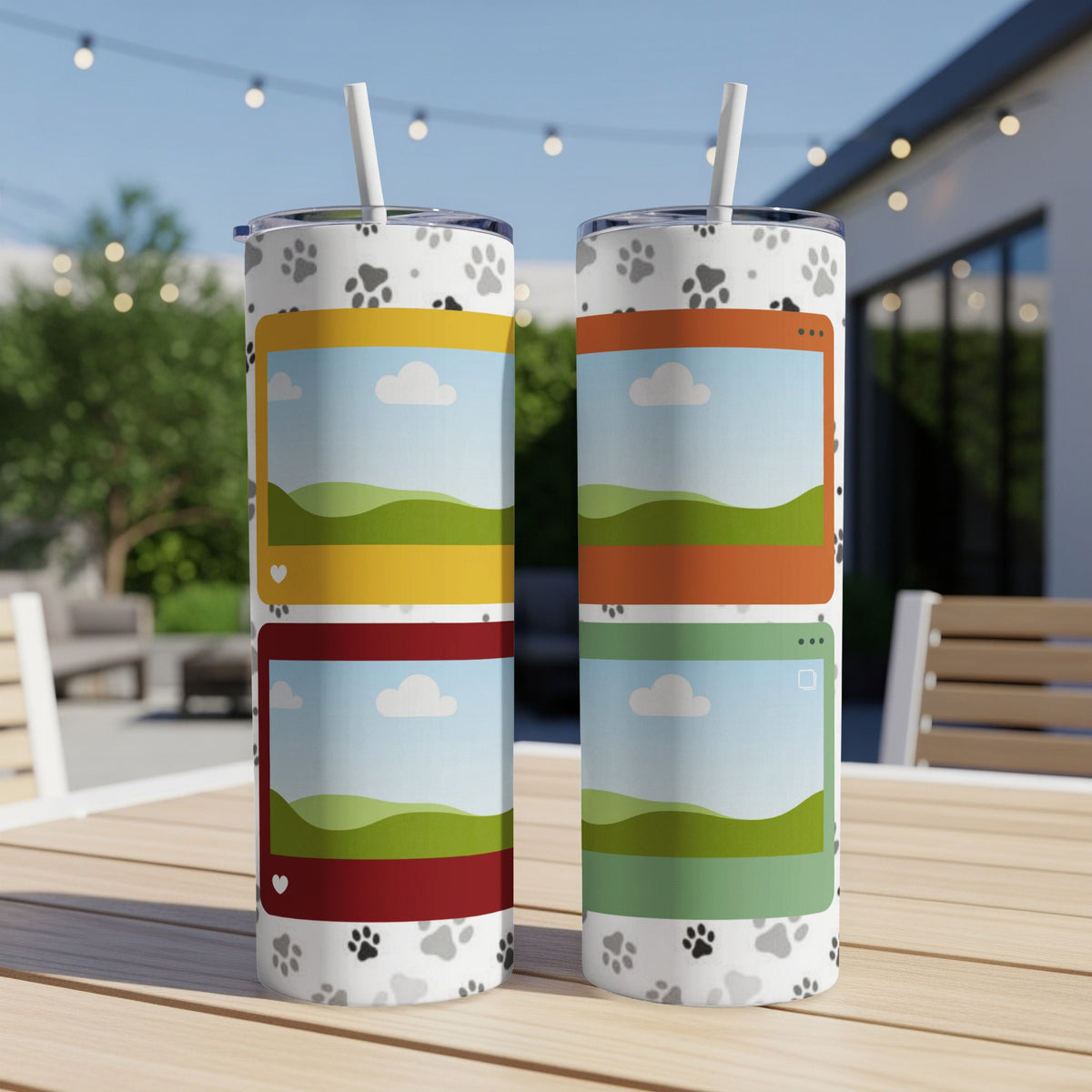 Two tumblers with paw prints and colorful landscape designs sit on a table outdoors.