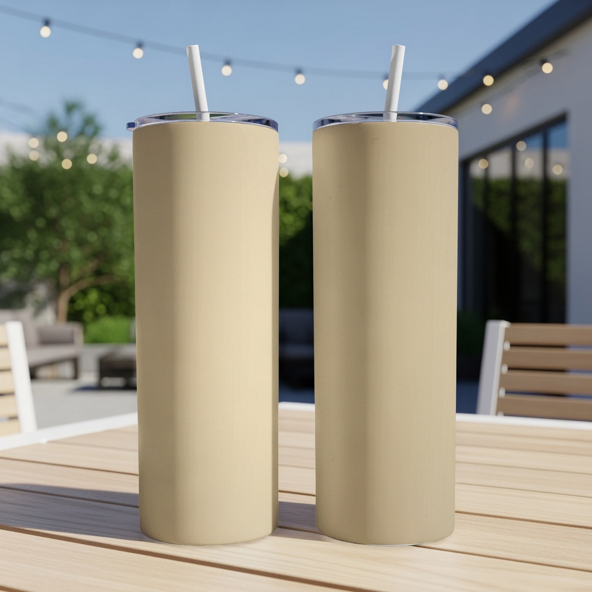Two tan tumblers with straws on a wooden table outdoors.