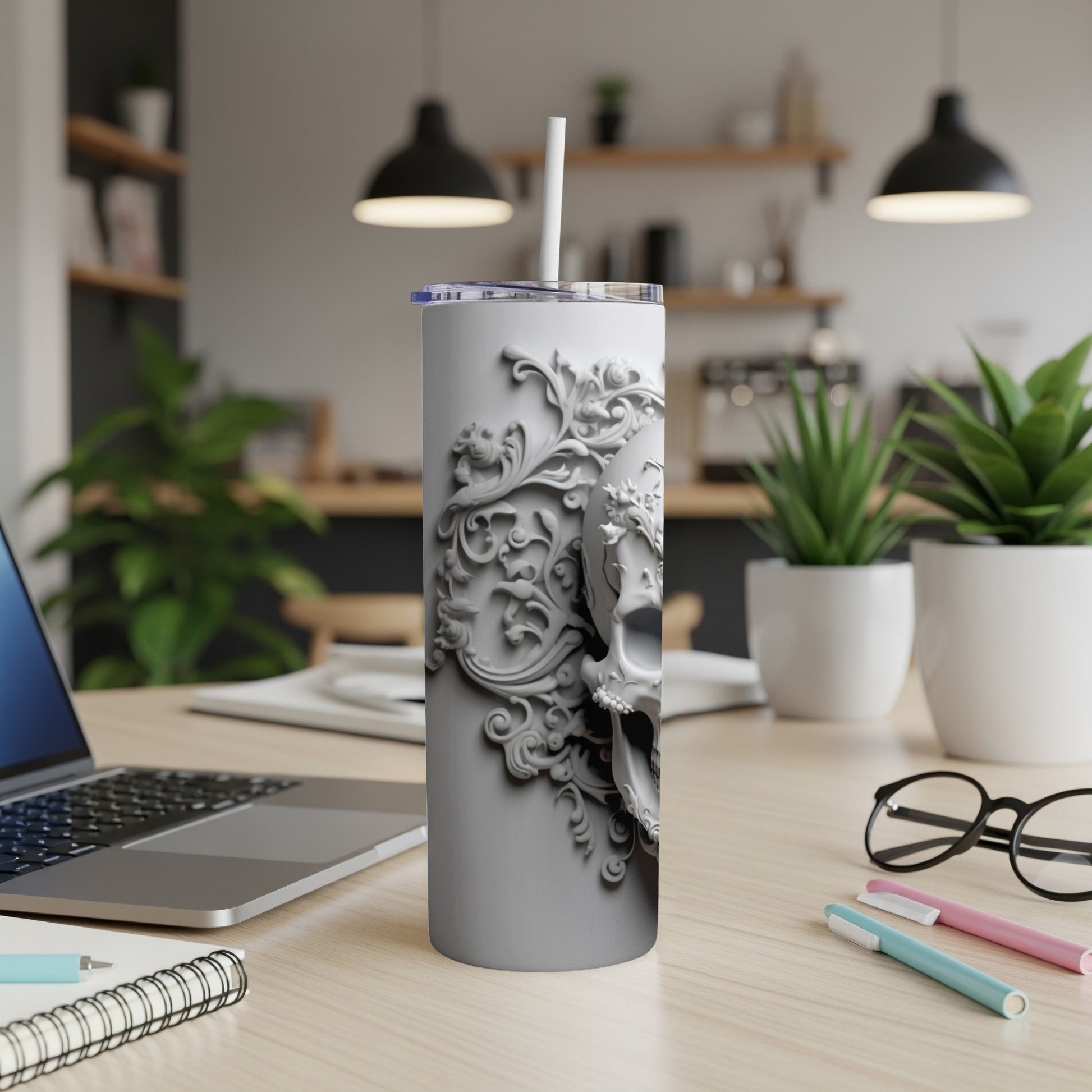White tumbler with intricate skull and floral relief design on desk.