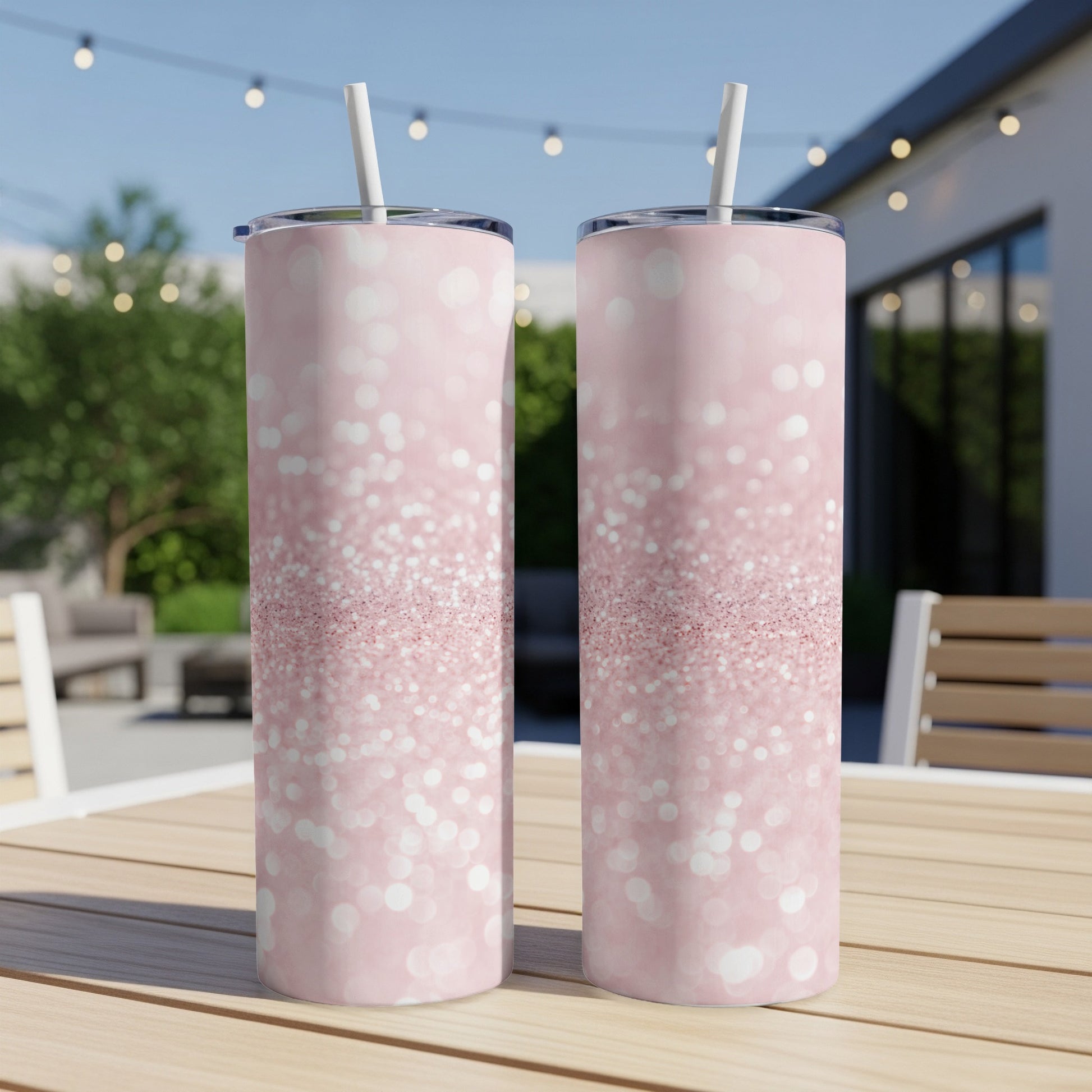 Two tall pink glitter tumblers with straws on a wooden table.