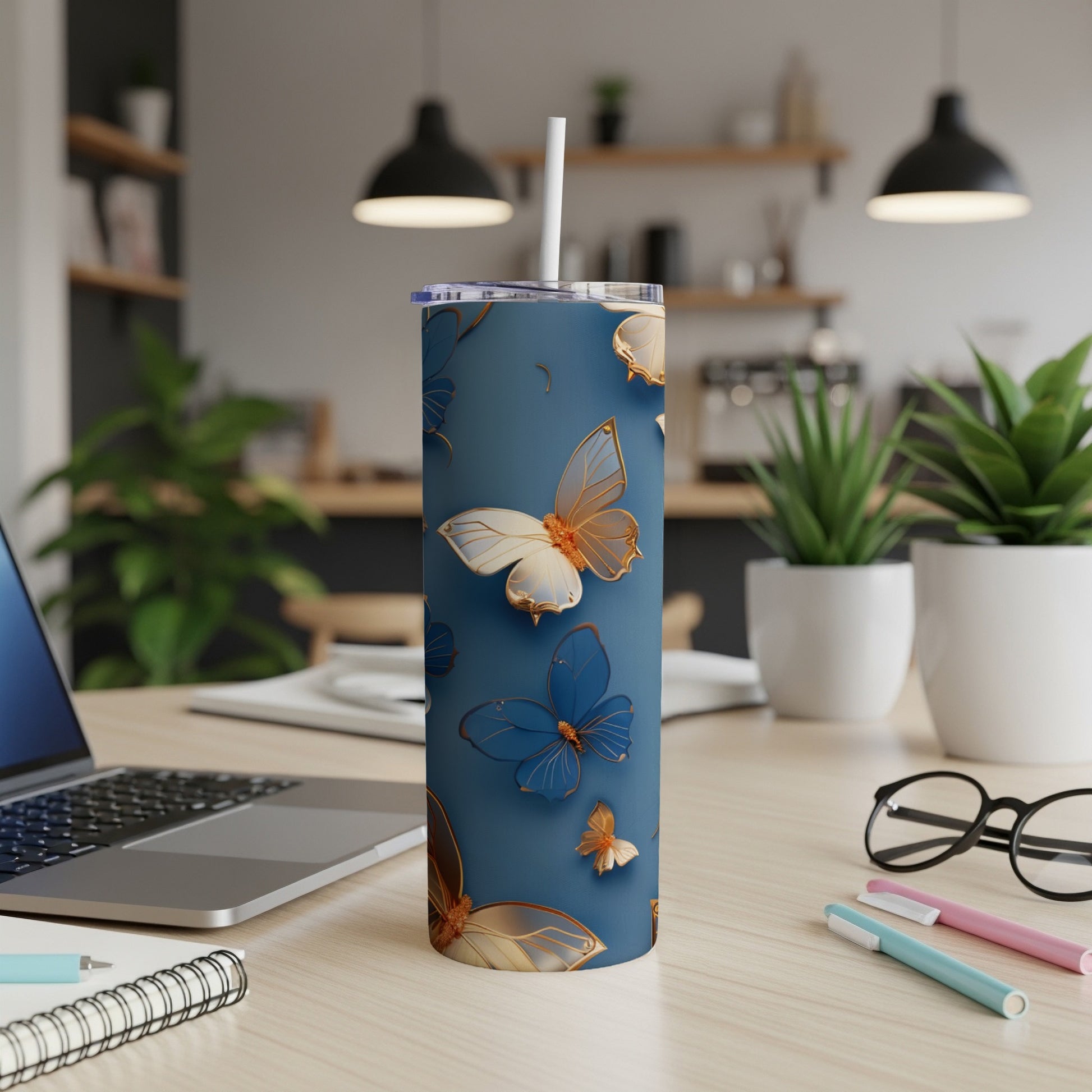 Blue tumbler with gold butterflies on a desk with a laptop and pens.
