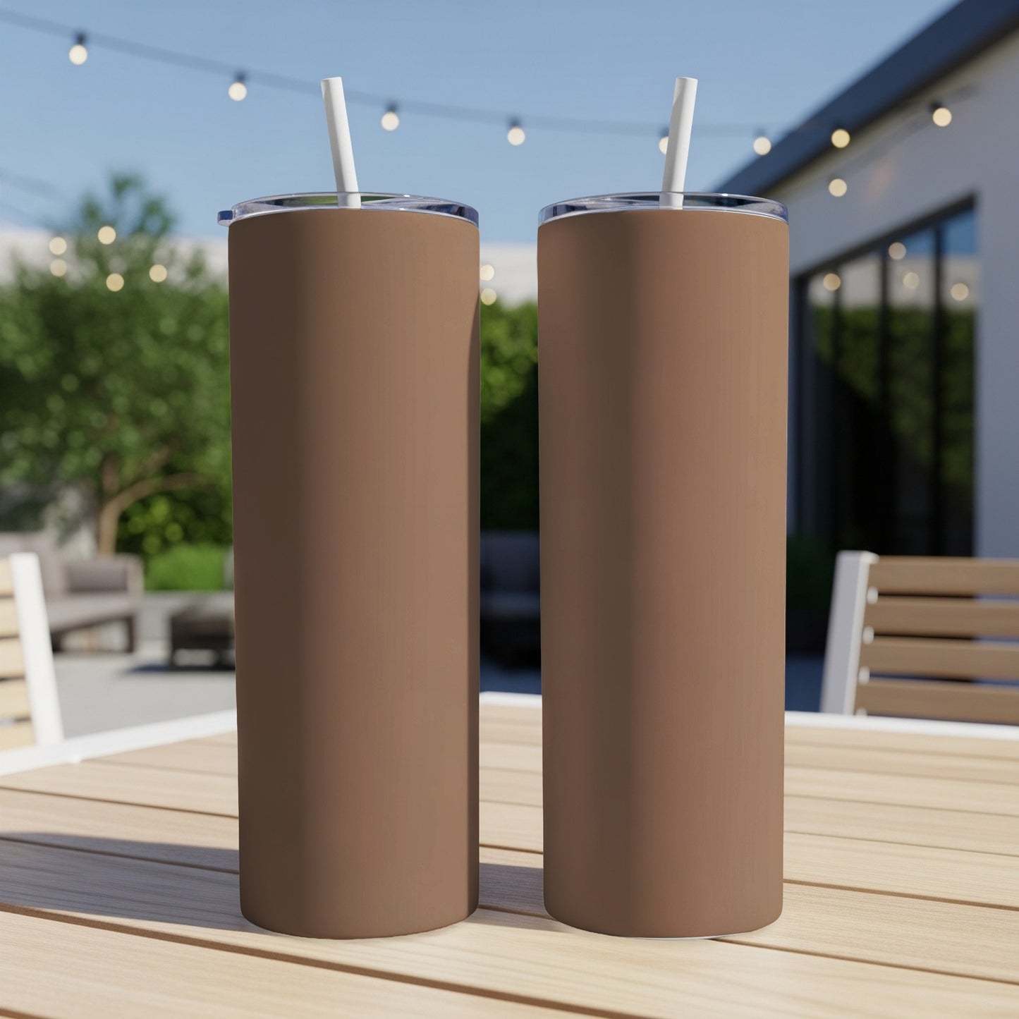 Two brown tumblers with white straws sit on a wooden table outdoors.