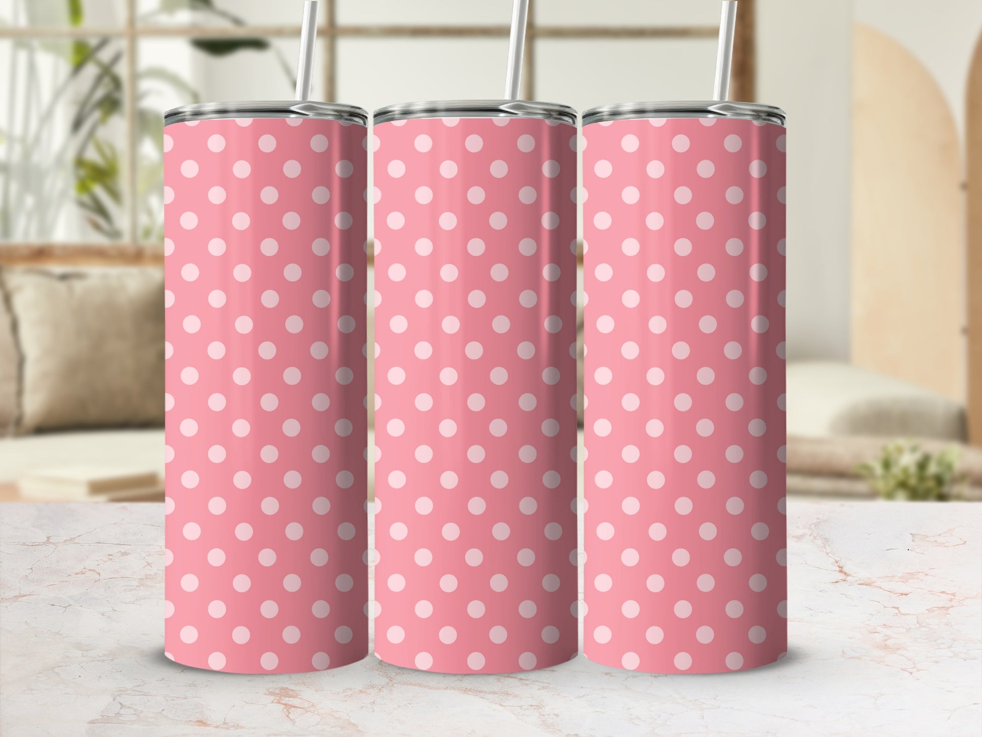Three pink tumblers with white polka dots and metal straws displayed on a marble surface.