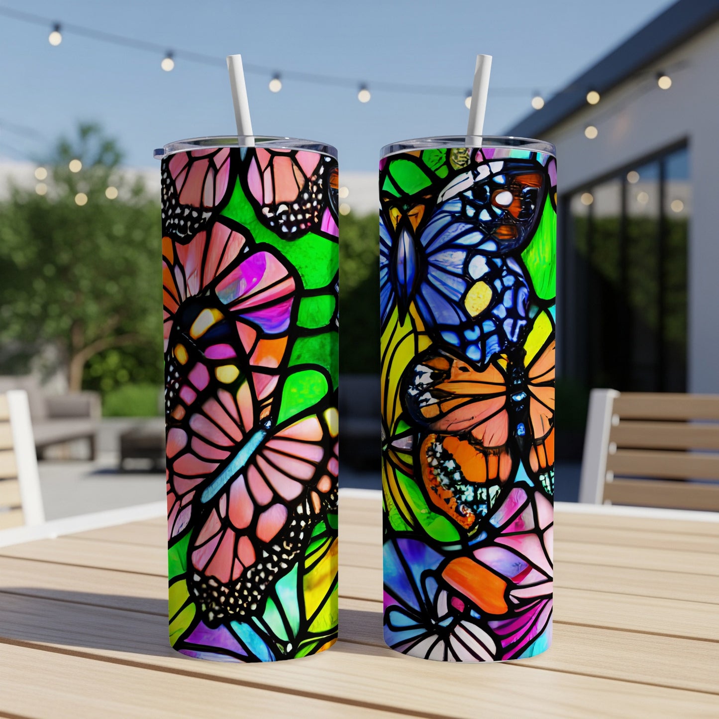 Two colorful butterfly stained-glass patterned tumblers with straws on a wooden table.