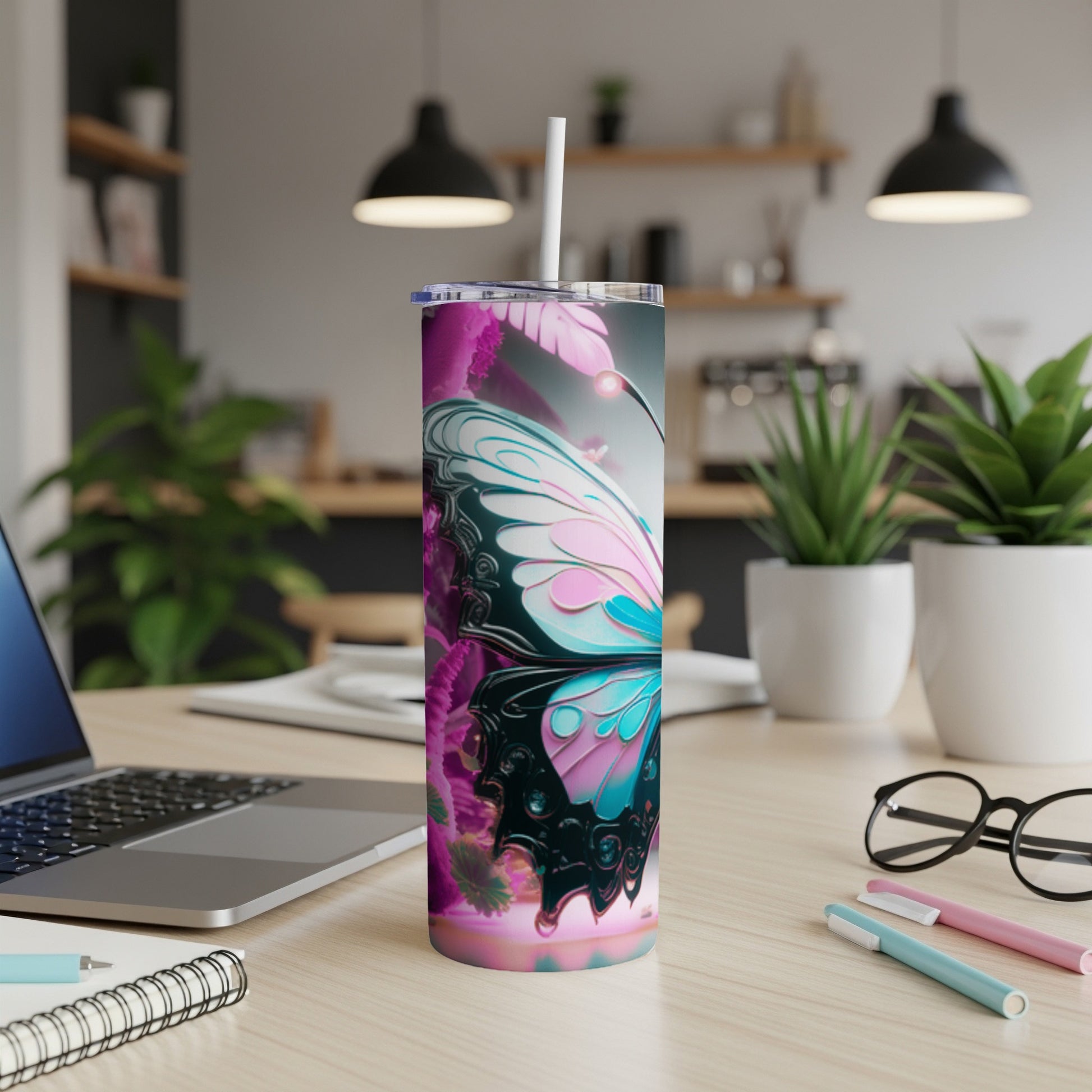 Tumbler with butterfly wing design, laptop, and pens on a desk.