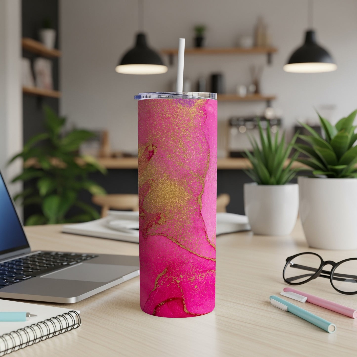 Pink and gold marbled skinny tumbler with straw on a desk.