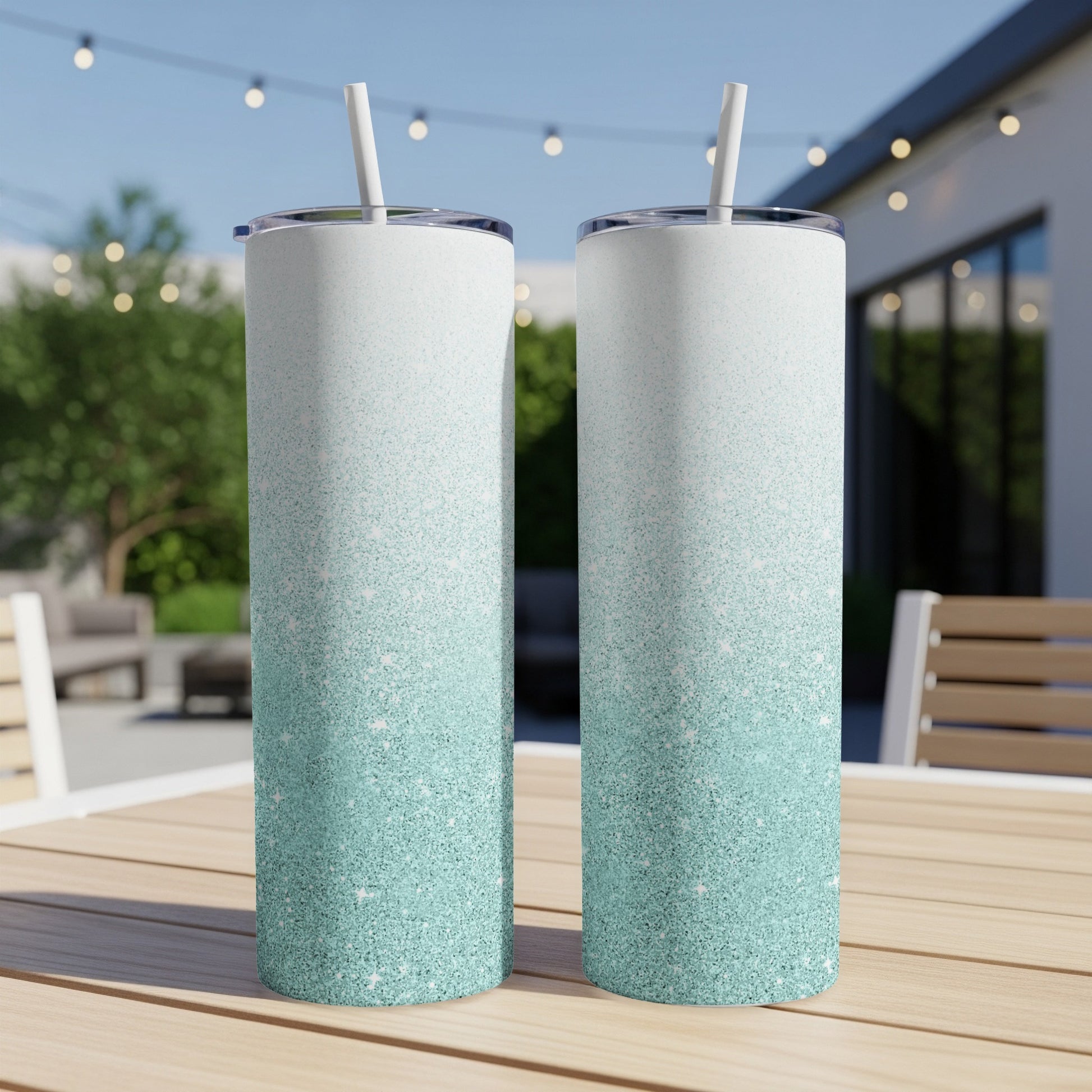 Two tall, skinny tumblers with teal and white glitter gradient on a table.