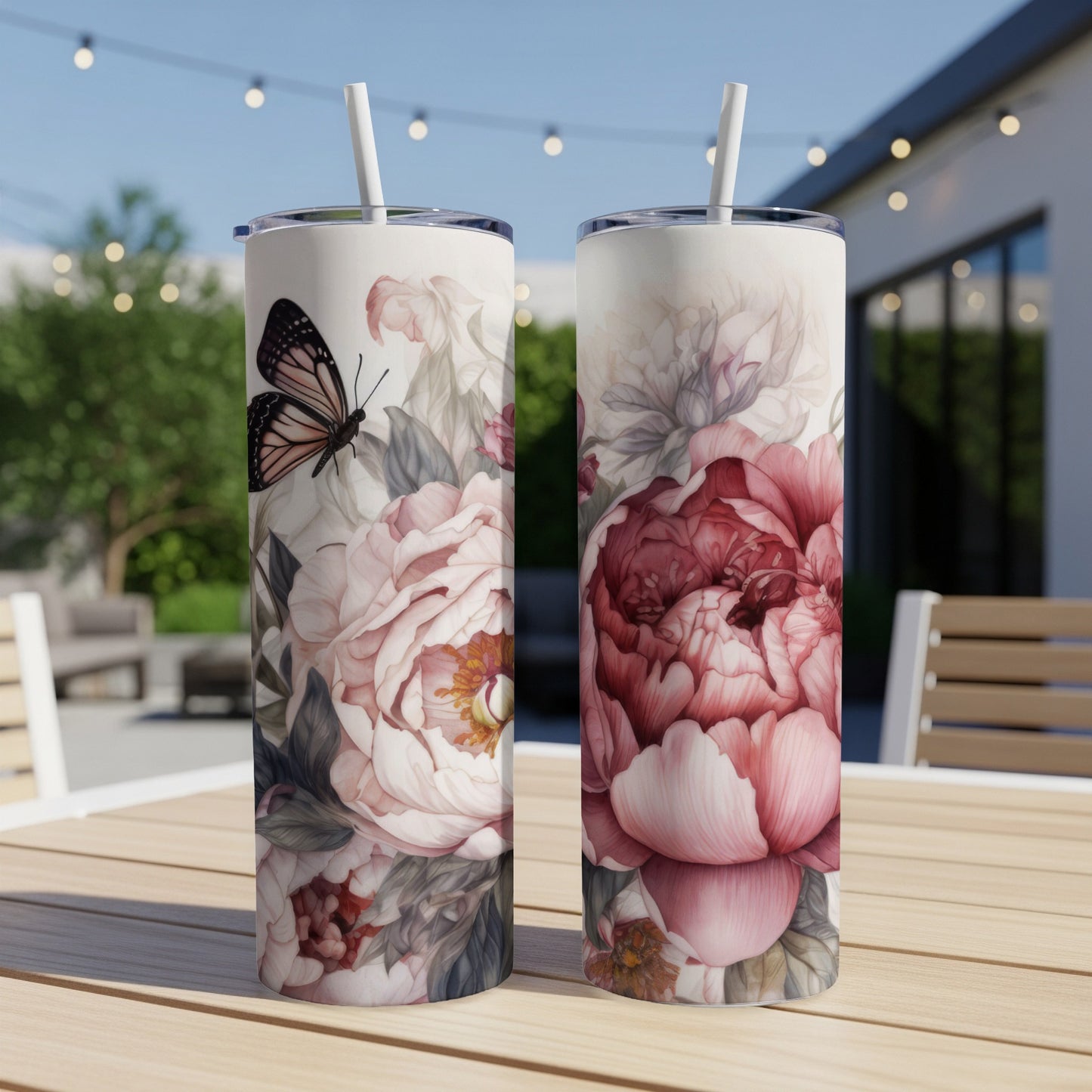 Two tumblers with floral and butterfly art on a wooden table outdoors.